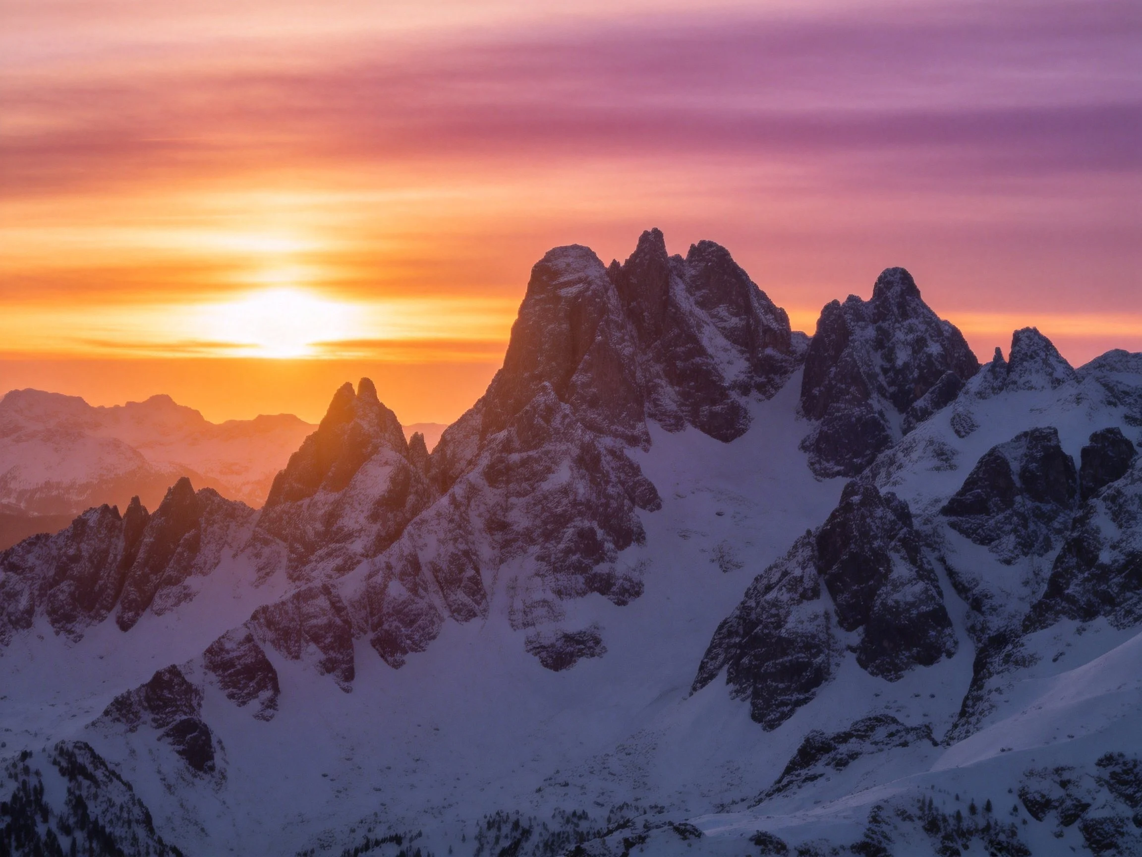 Snow-capped mountain peaks at vibrant sunset with purple and orange sky