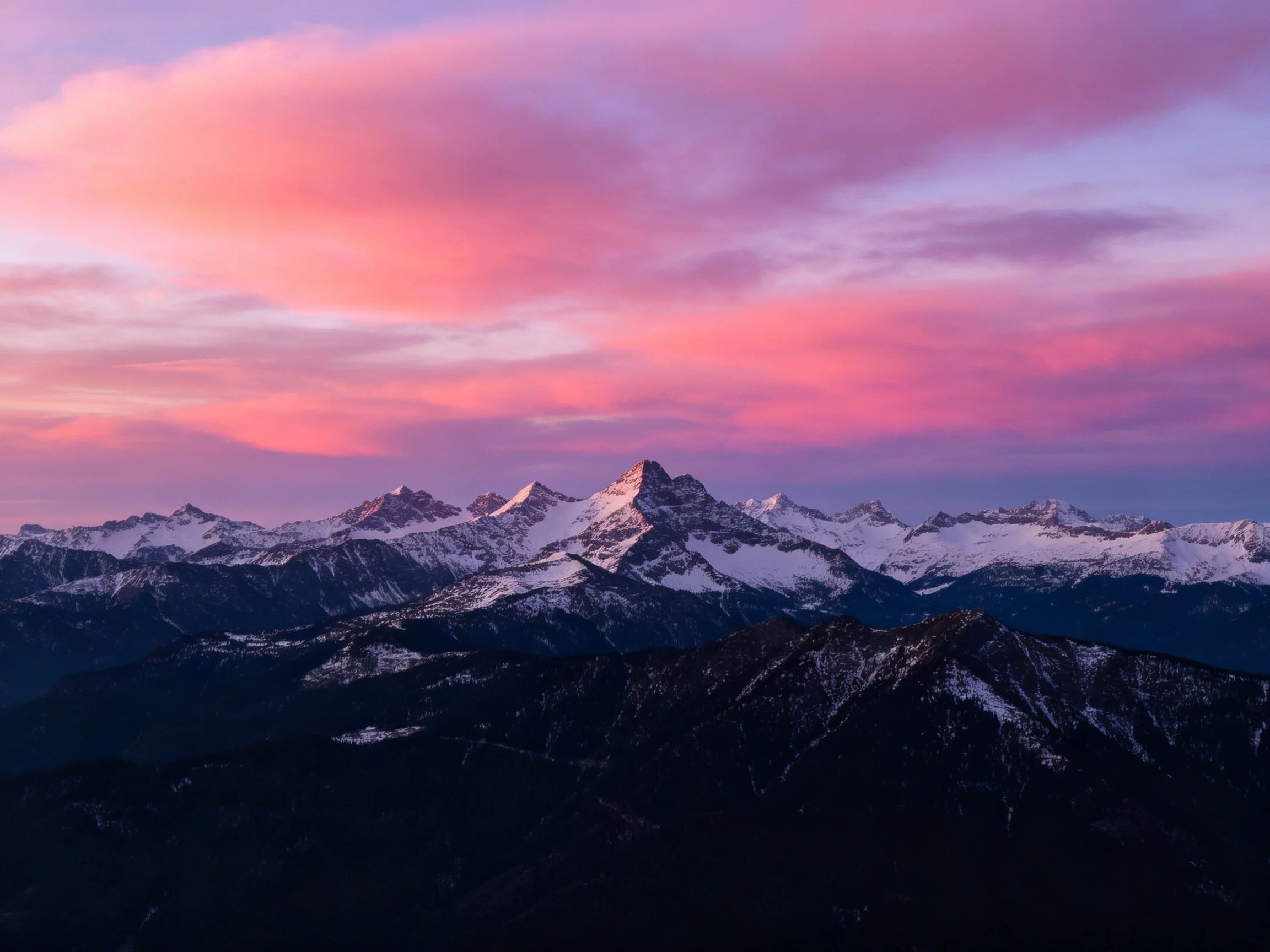 Snow-capped mountain peaks beneath vibrant pink-purple twilight sky