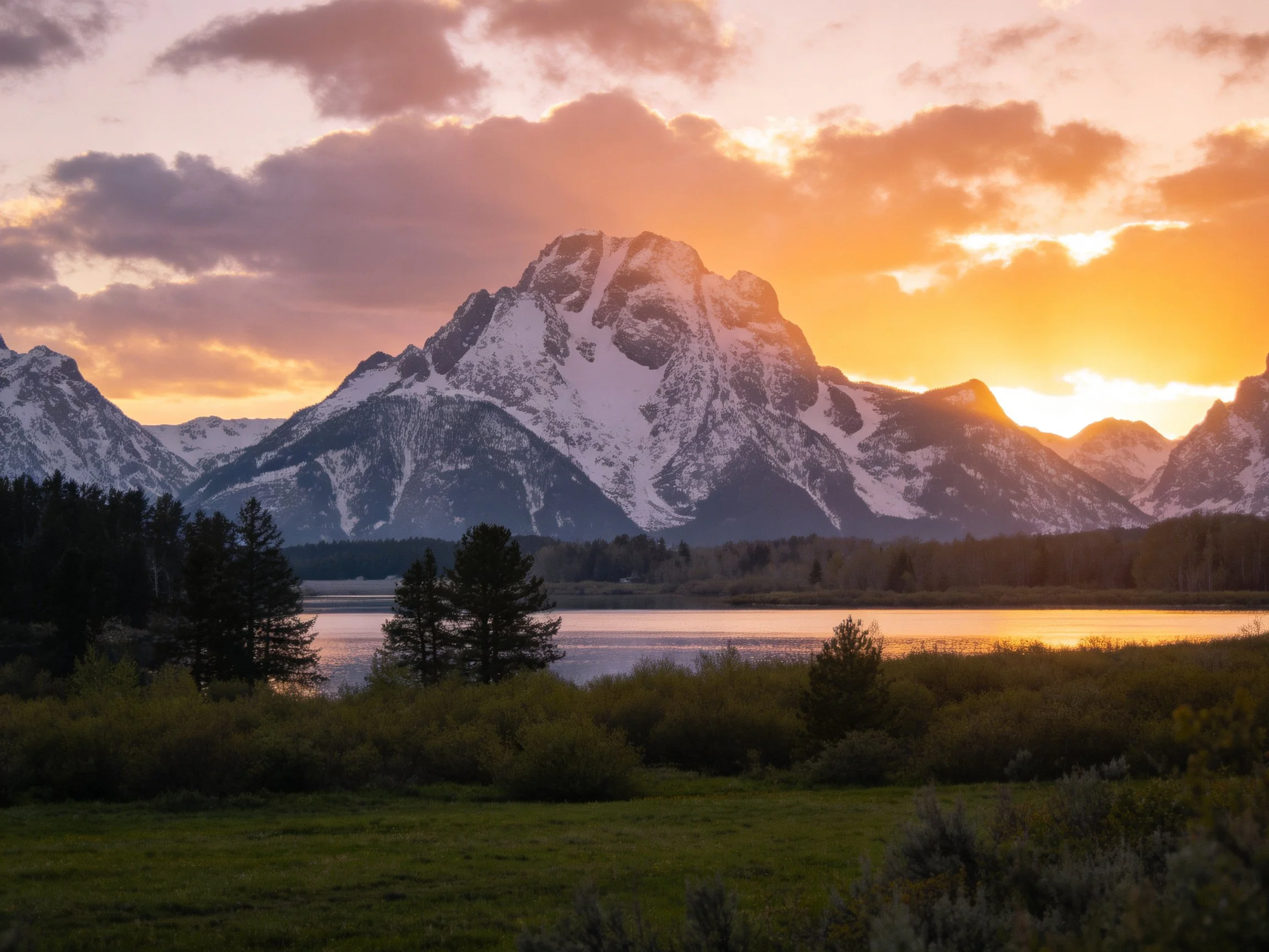 Snow - capped mountain peaks glow under vibrant sunset skies