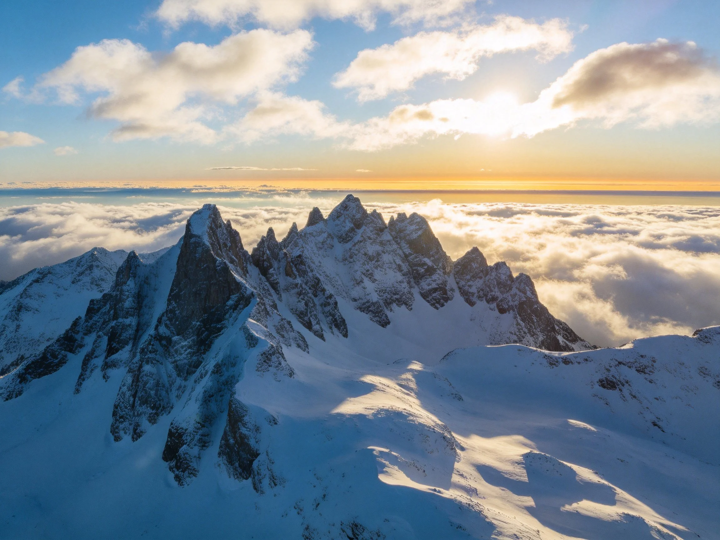 Snow-capped mountain peaks rising above cloud sea at sunrise