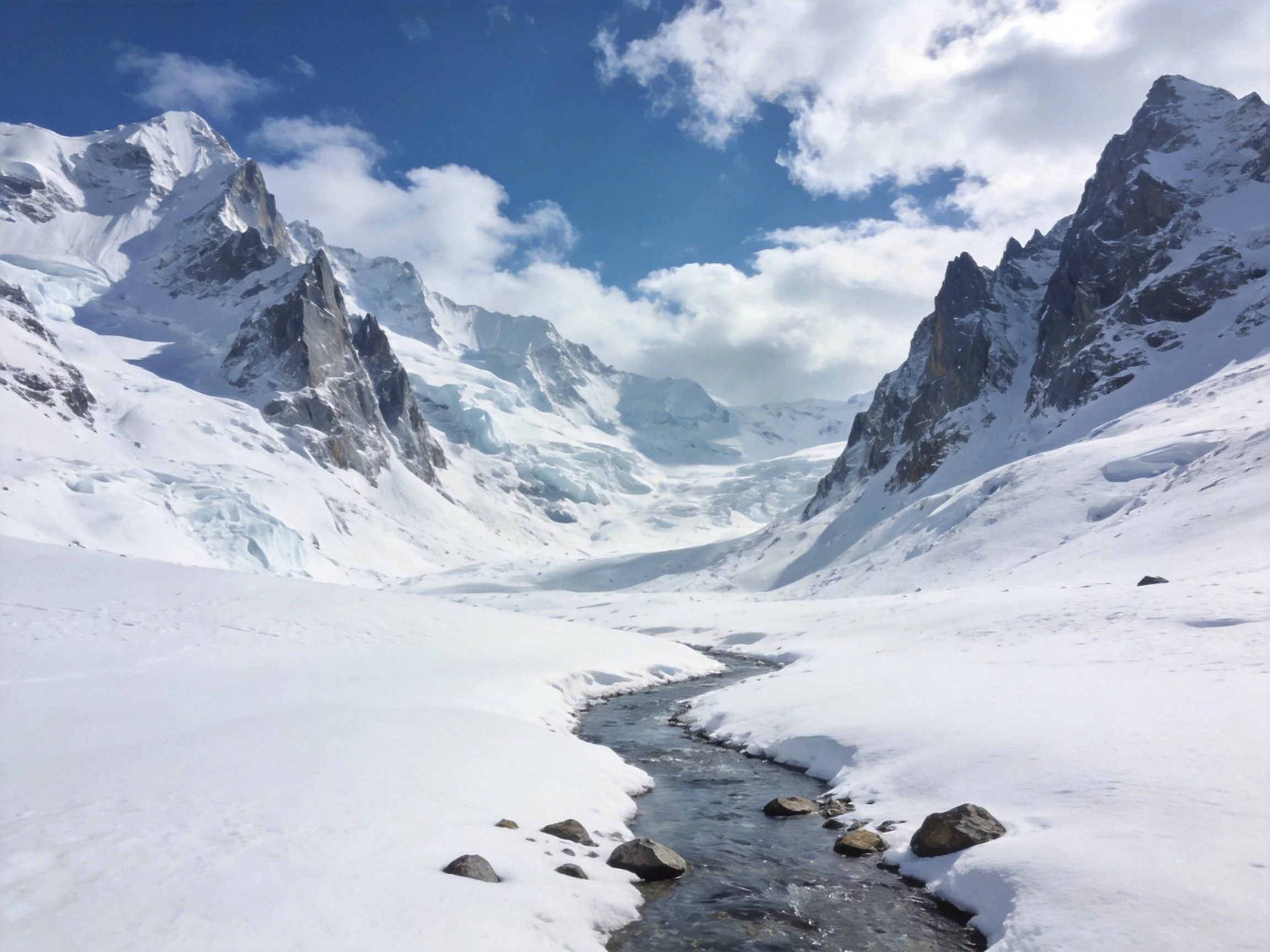 Snow-capped mountain peaks, winding stream, and bright blue sky