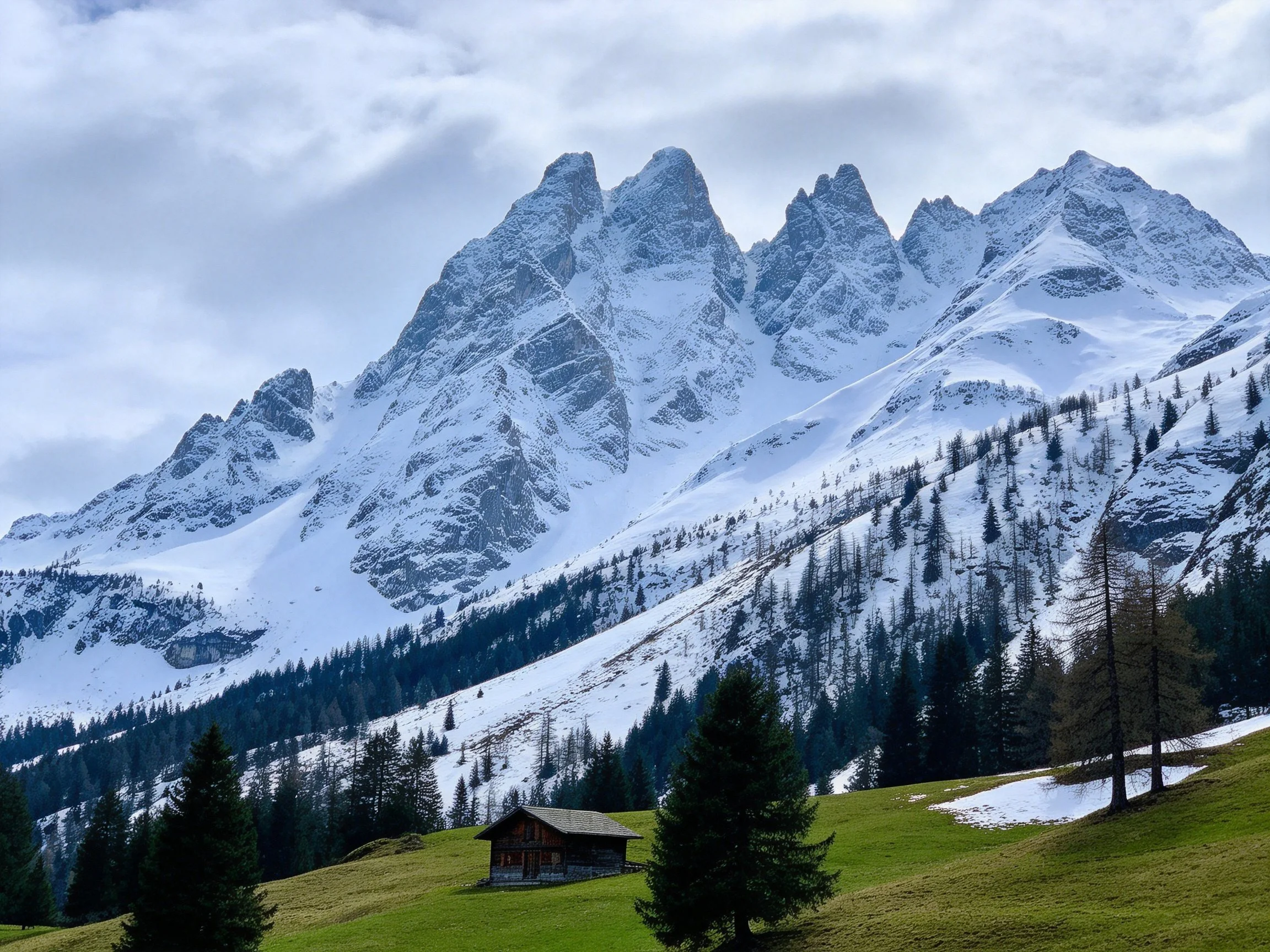 Snow - capped mountain peaks with a wooden cabin in a green meadow