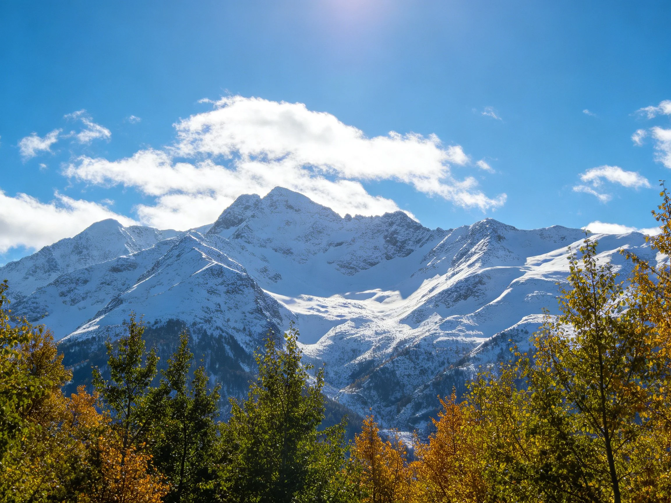 Snow-capped mountain peaks with autumnal trees and bright blue sky