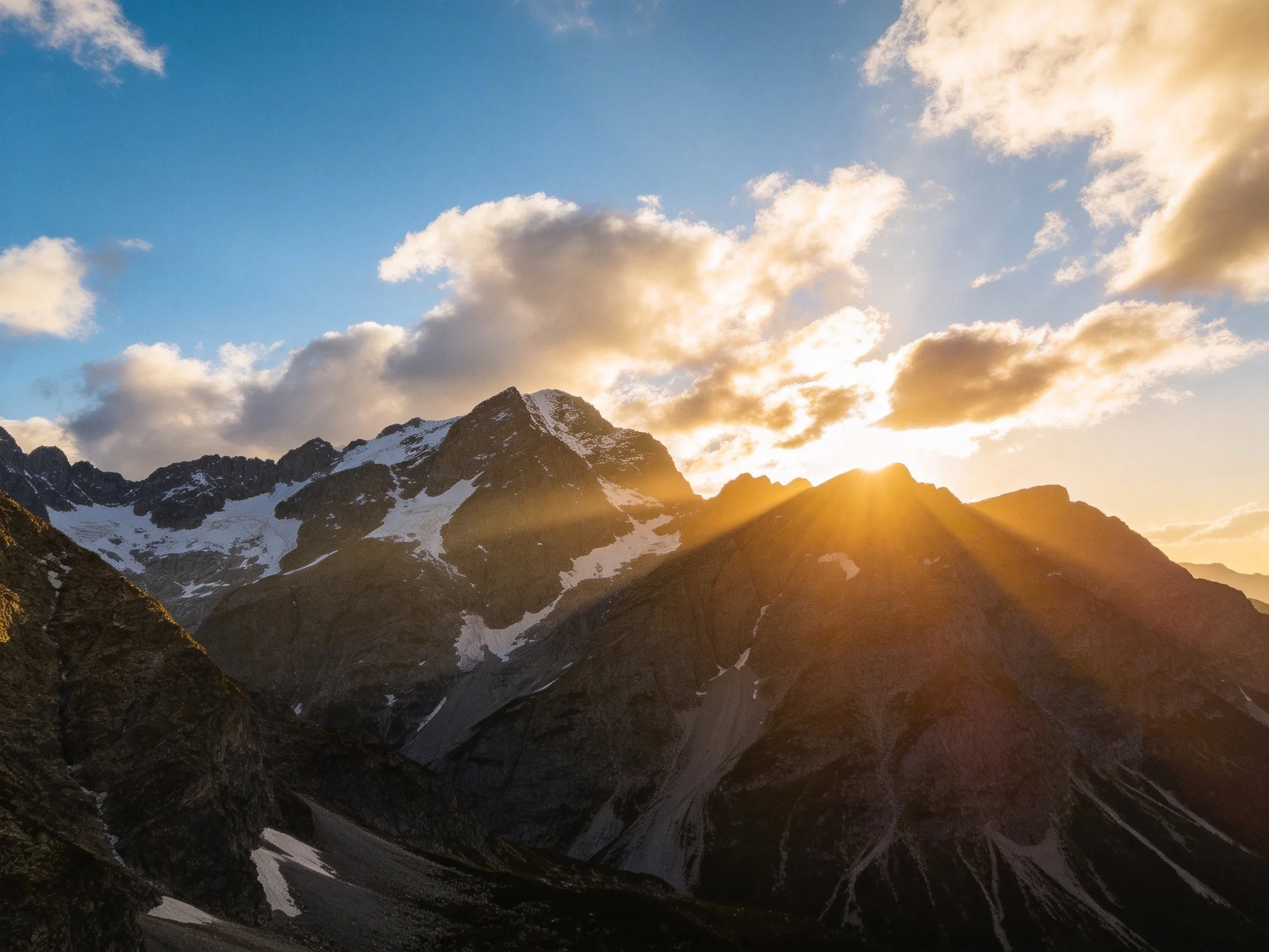 Snow-capped mountain peaks with golden sunset and cloudy sky