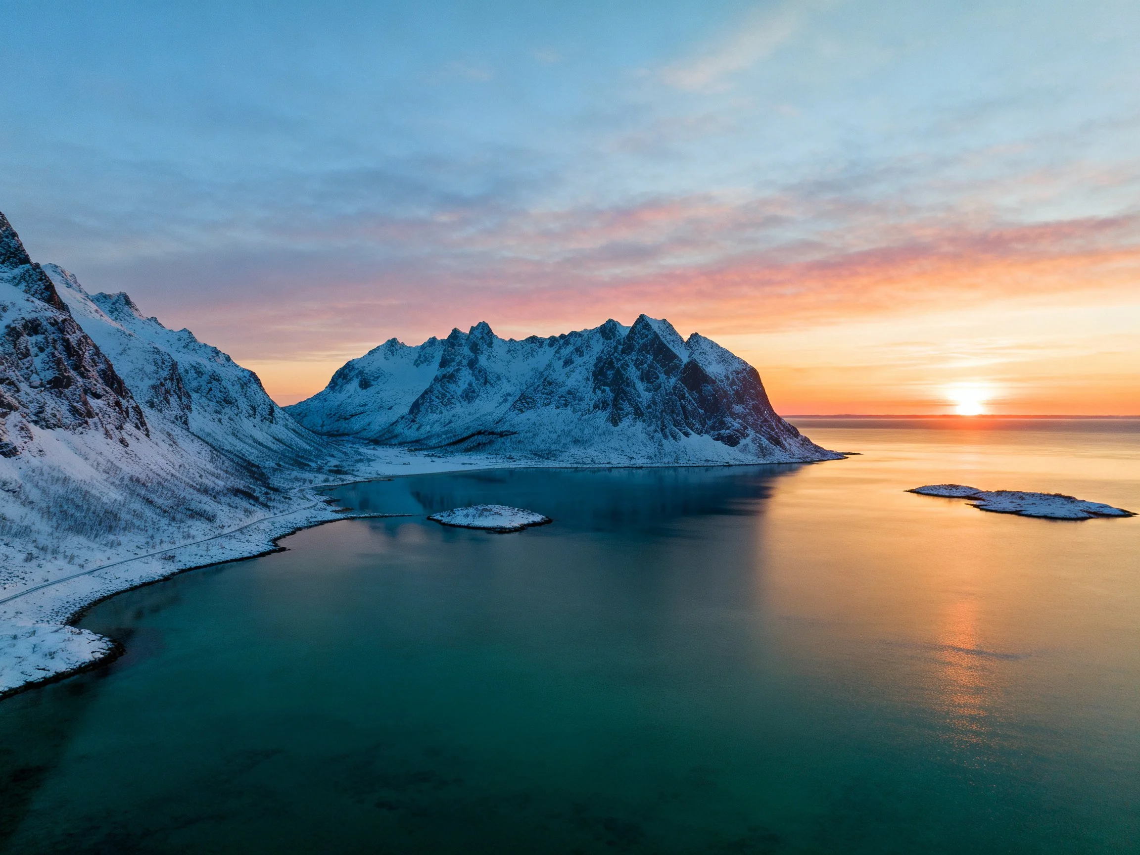 Snow-capped mountain range by turquoise waters at sunset