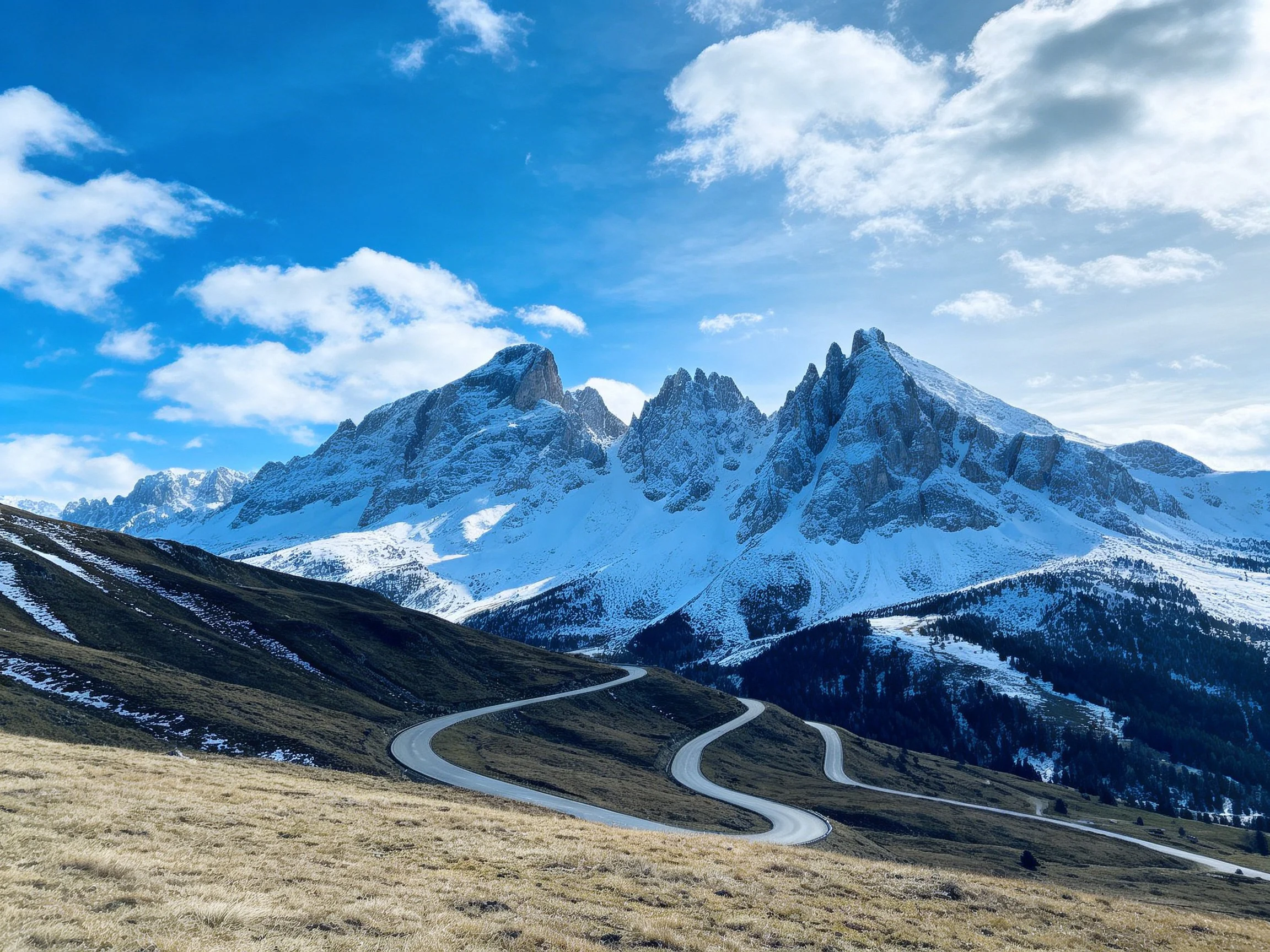 Snow - capped mountain range with winding road and clear blue sky