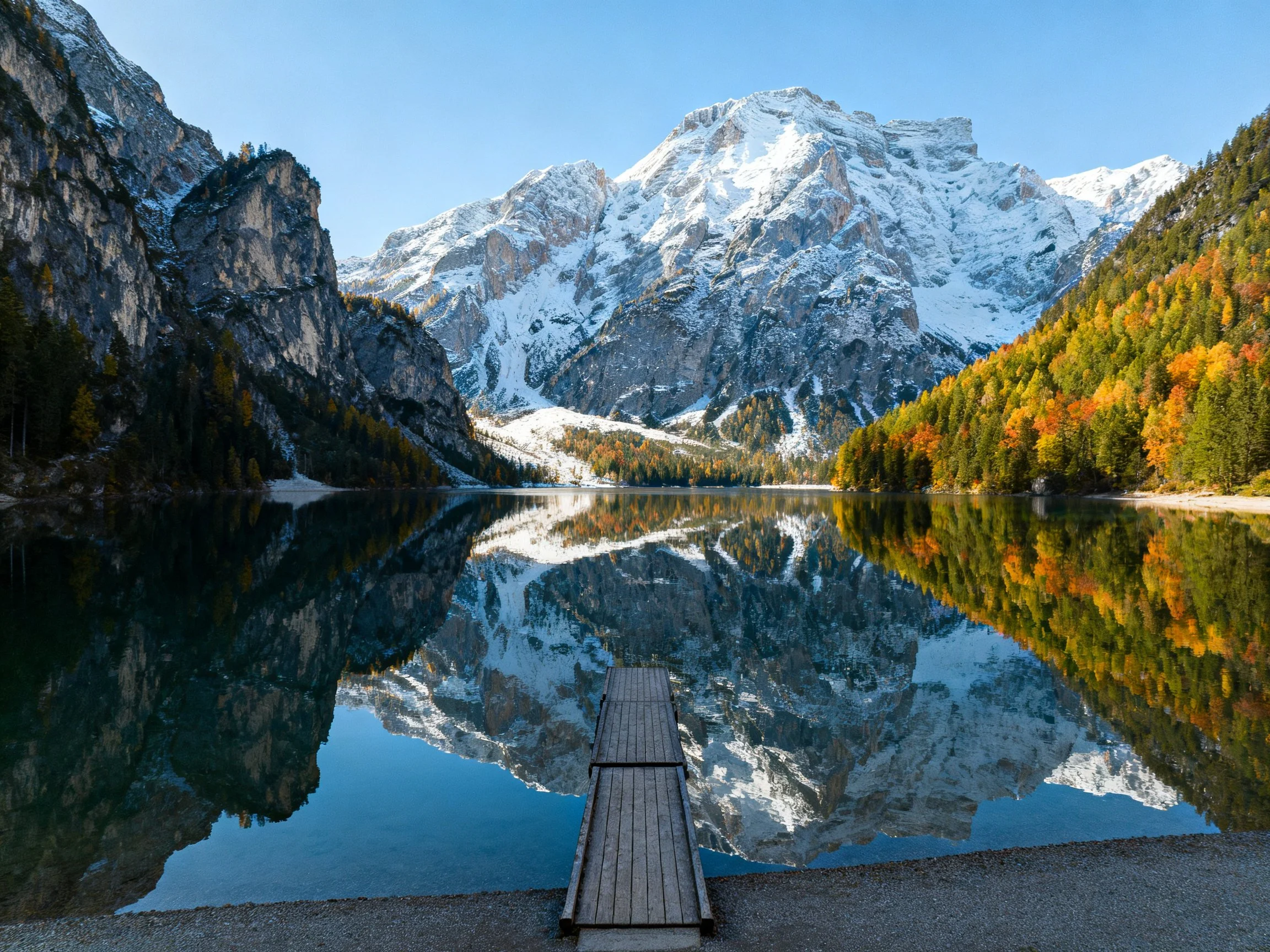 Snow-capped mountain reflected in tranquil autumn lake with wooden dock