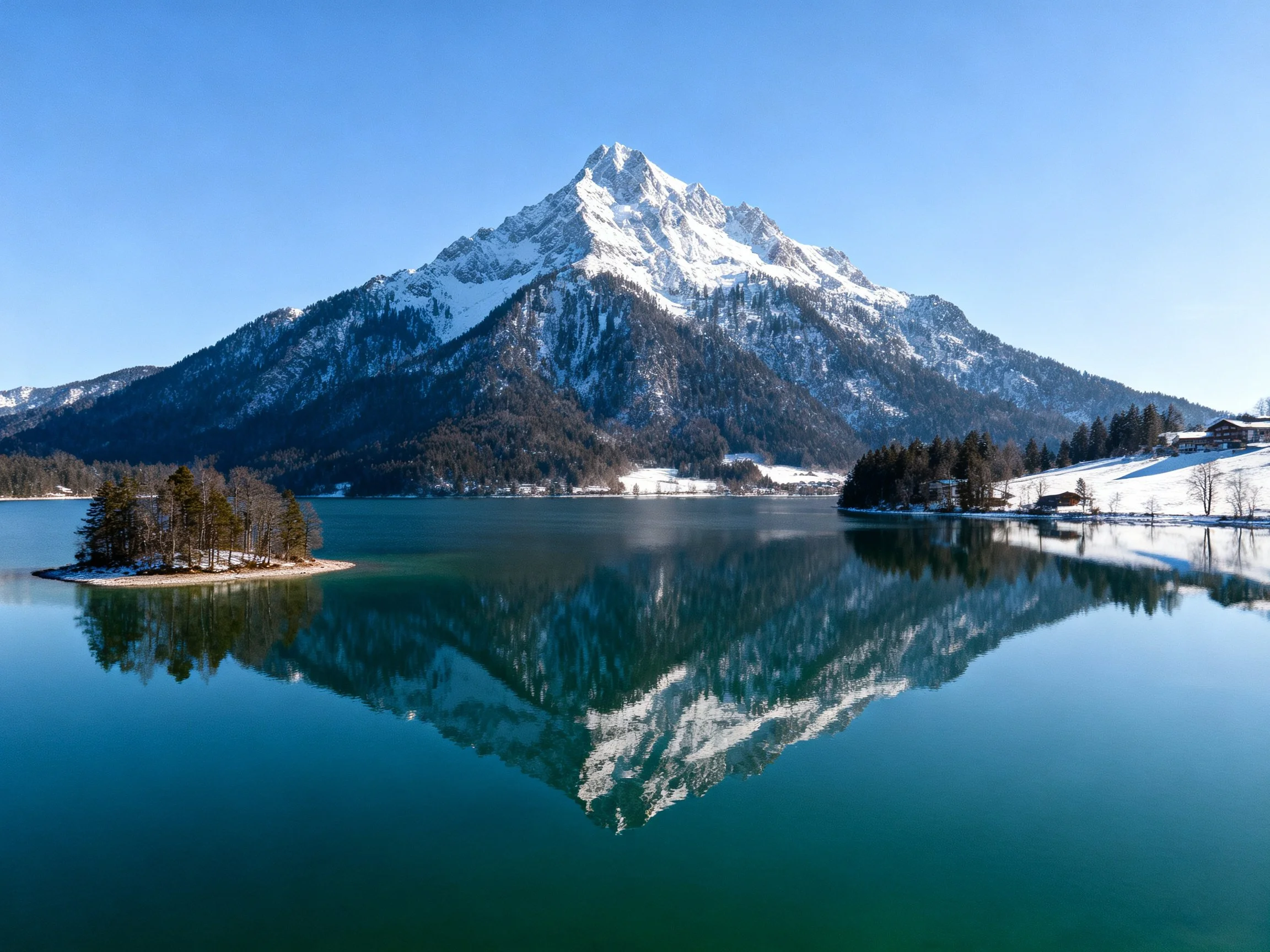 Snow-capped mountain reflects in tranquil blue lake with forested island