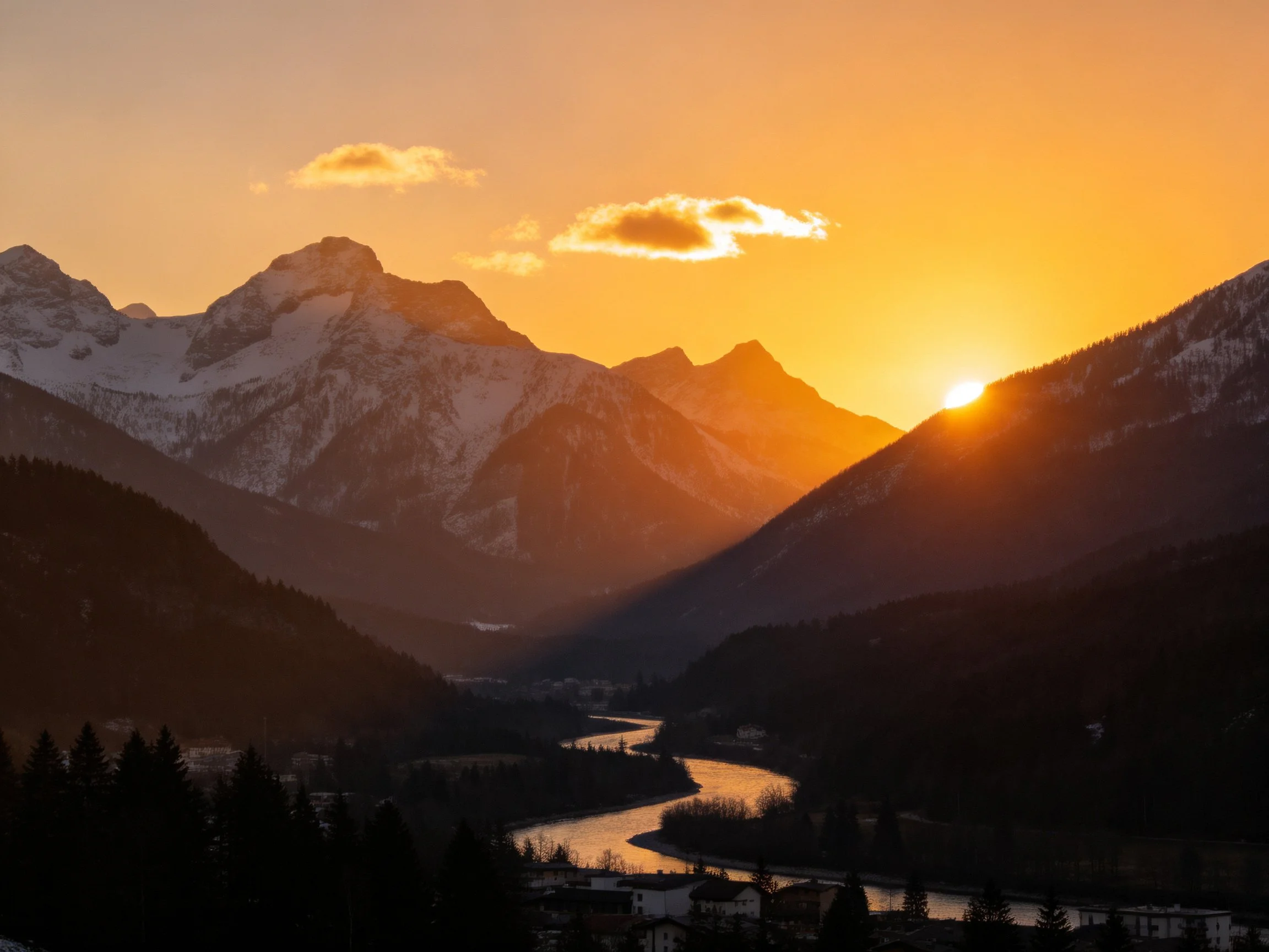 Snow-capped mountains at golden sunset over winding valley river