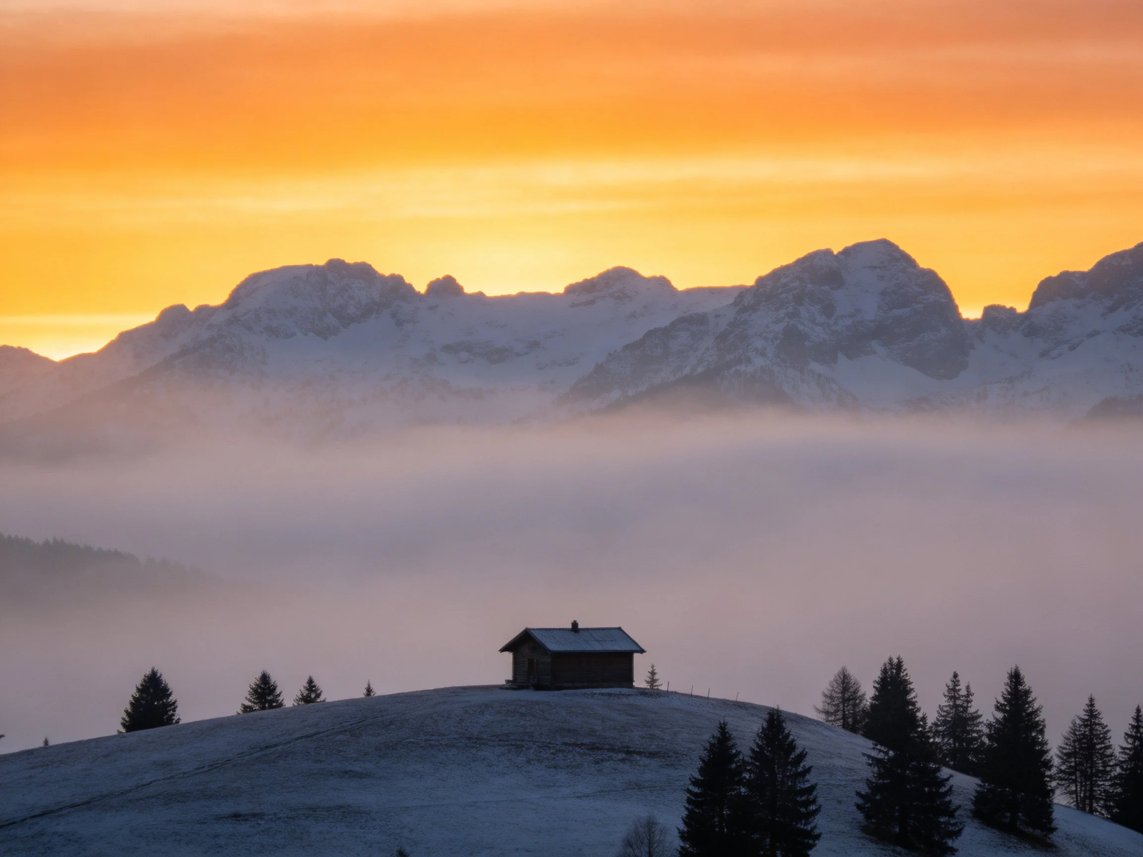 Snow-capped mountains behind foggy valley with wooden cabin
