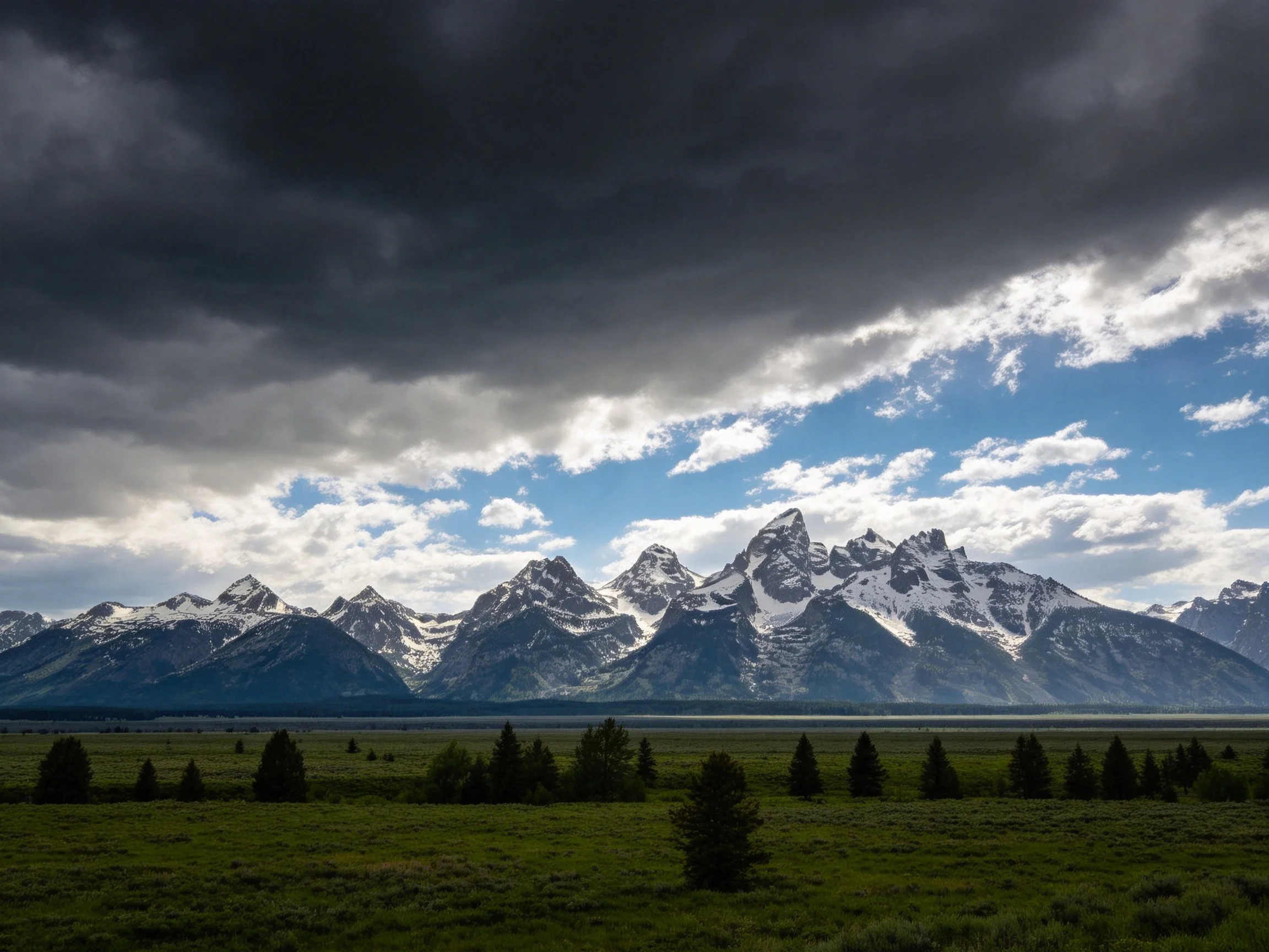 Snow-capped mountains beneath stormy skies with verdant valley