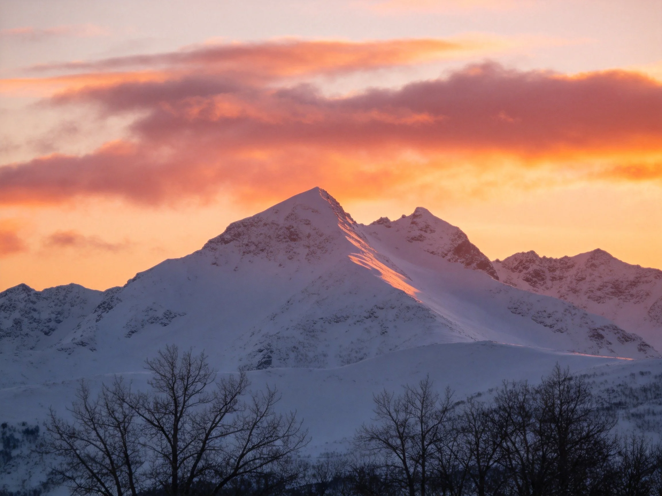 Snow-capped mountains beneath vibrant orange-pink sunset skies