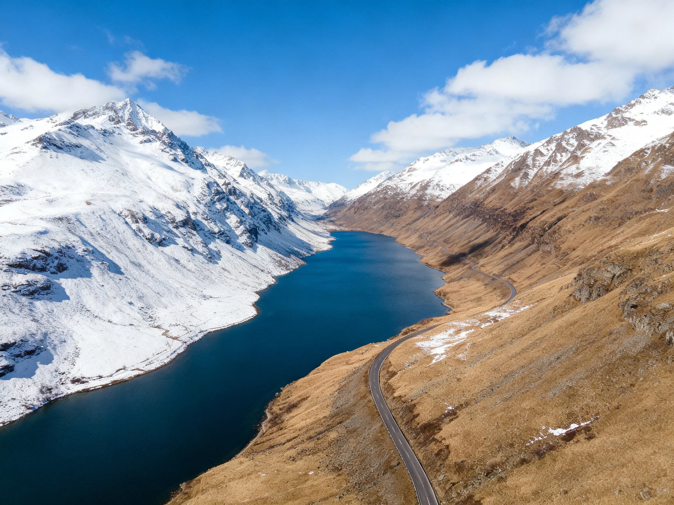 Snow - capped mountains border a deep blue lake with a winding road