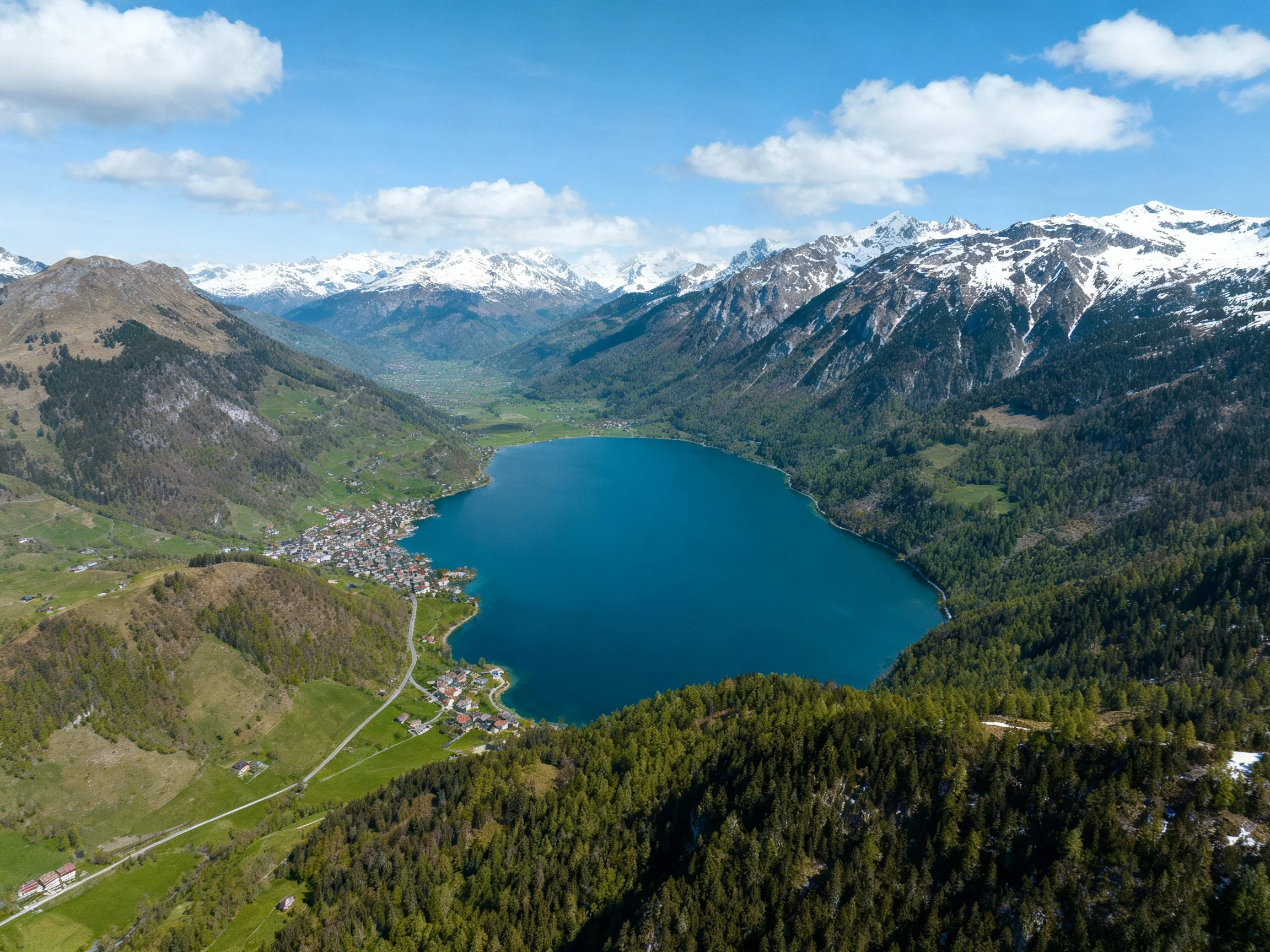 Snow-capped mountains encircle a vibrant blue alpine lake and forested valley