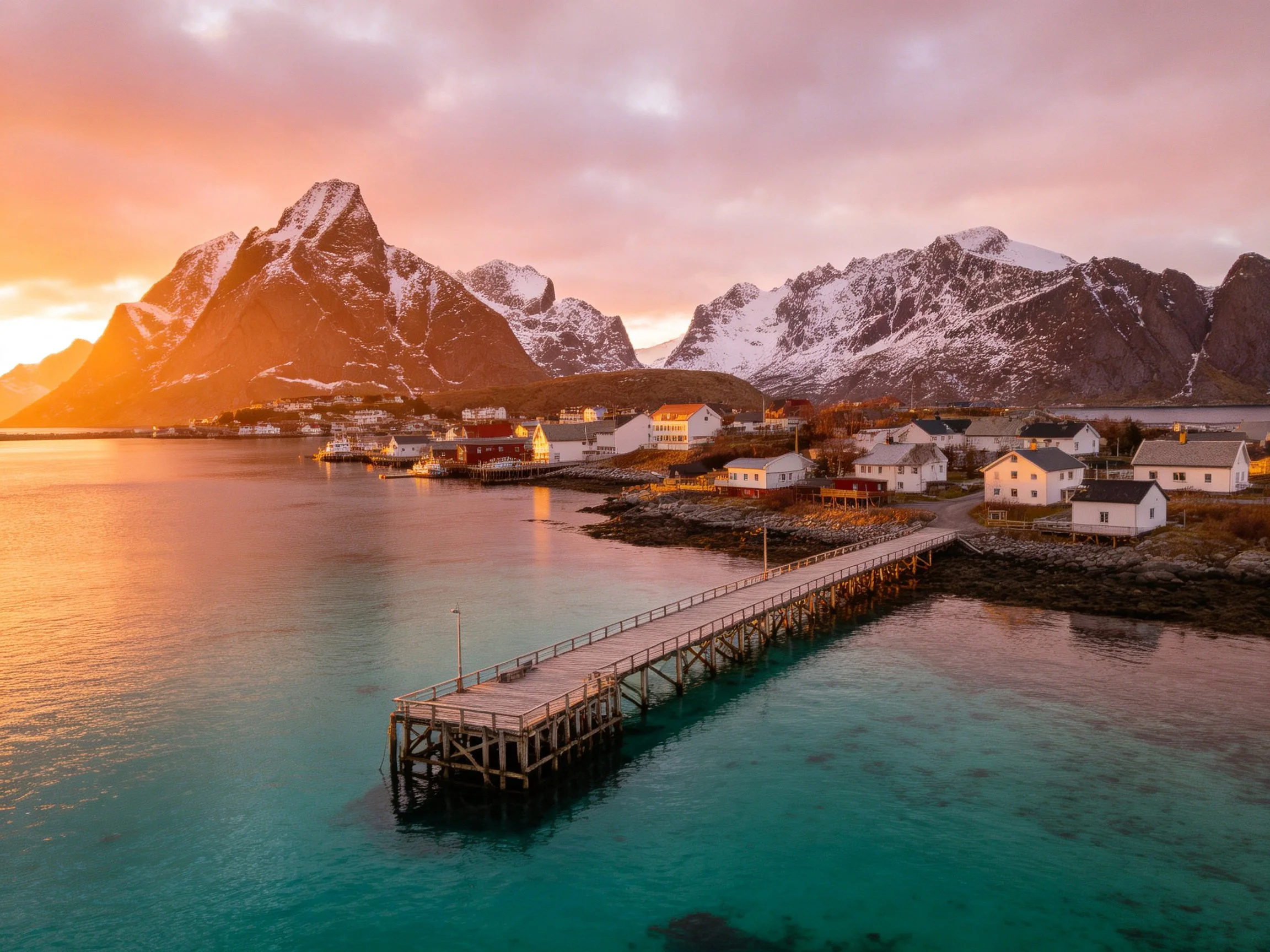 Snow-capped mountains frame a coastal village with turquoise waters