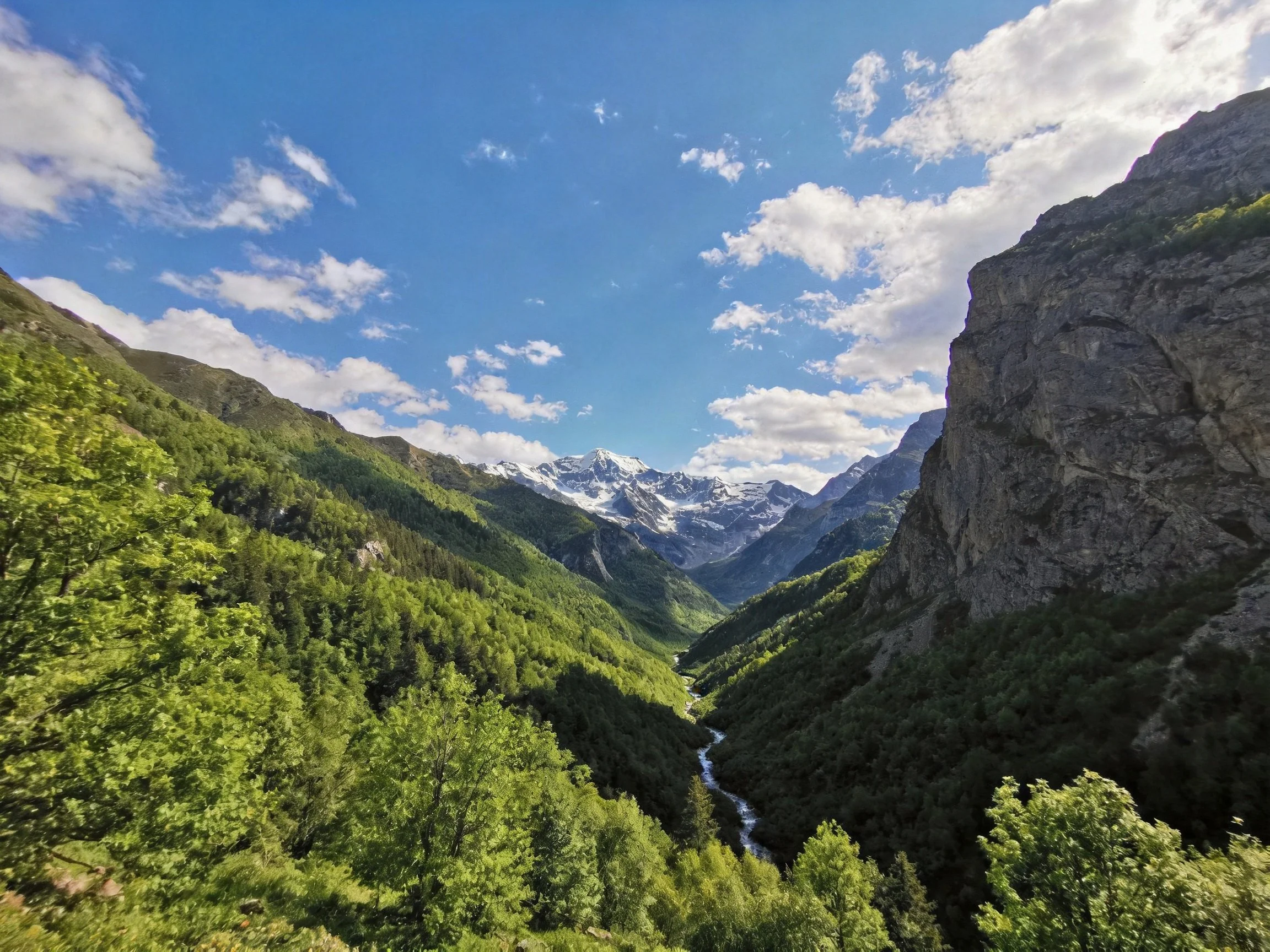 Snow - capped mountains frame a lush green valley with a winding stream