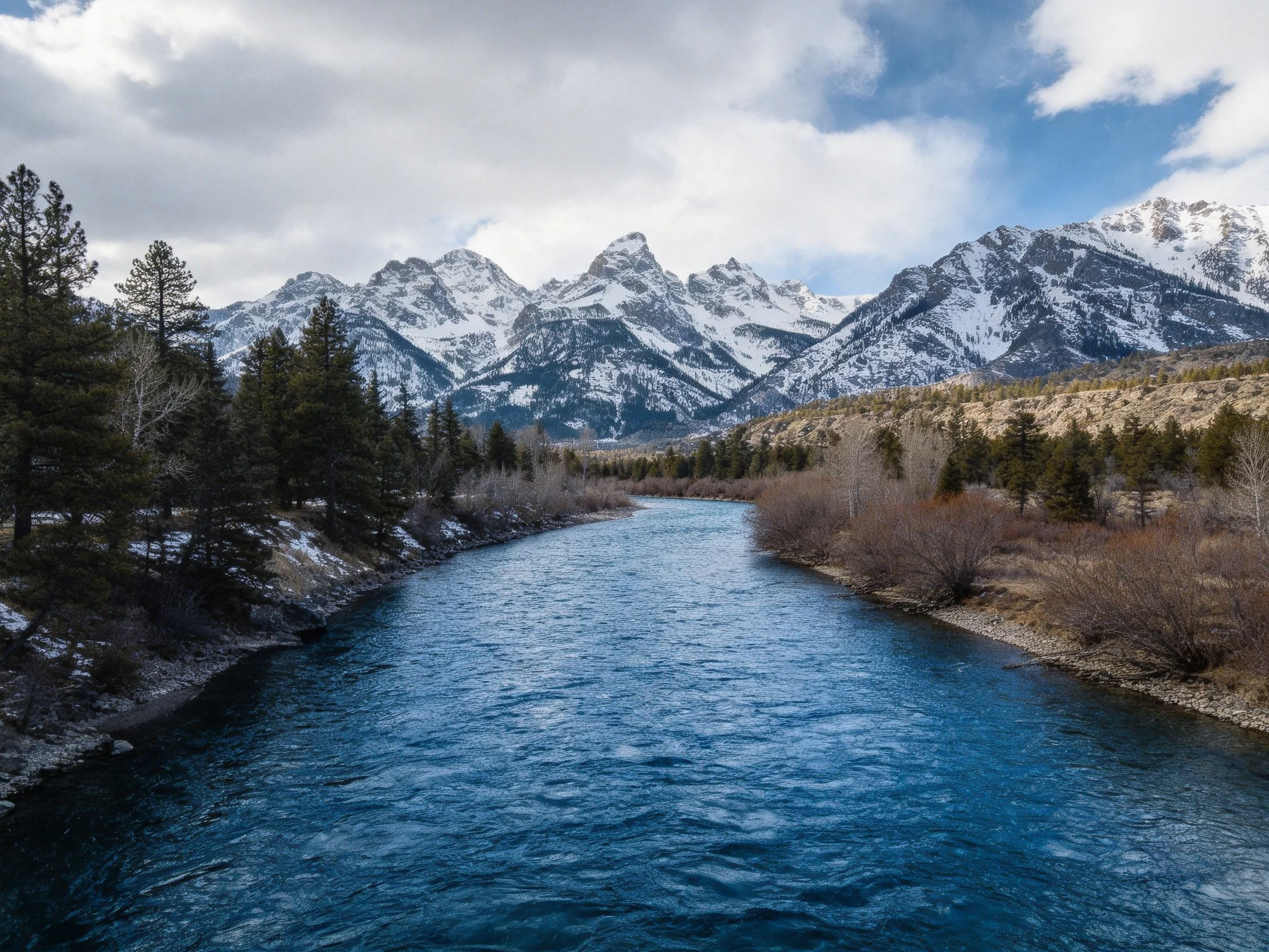 Snow-capped mountains frame a winding blue river with forested banks