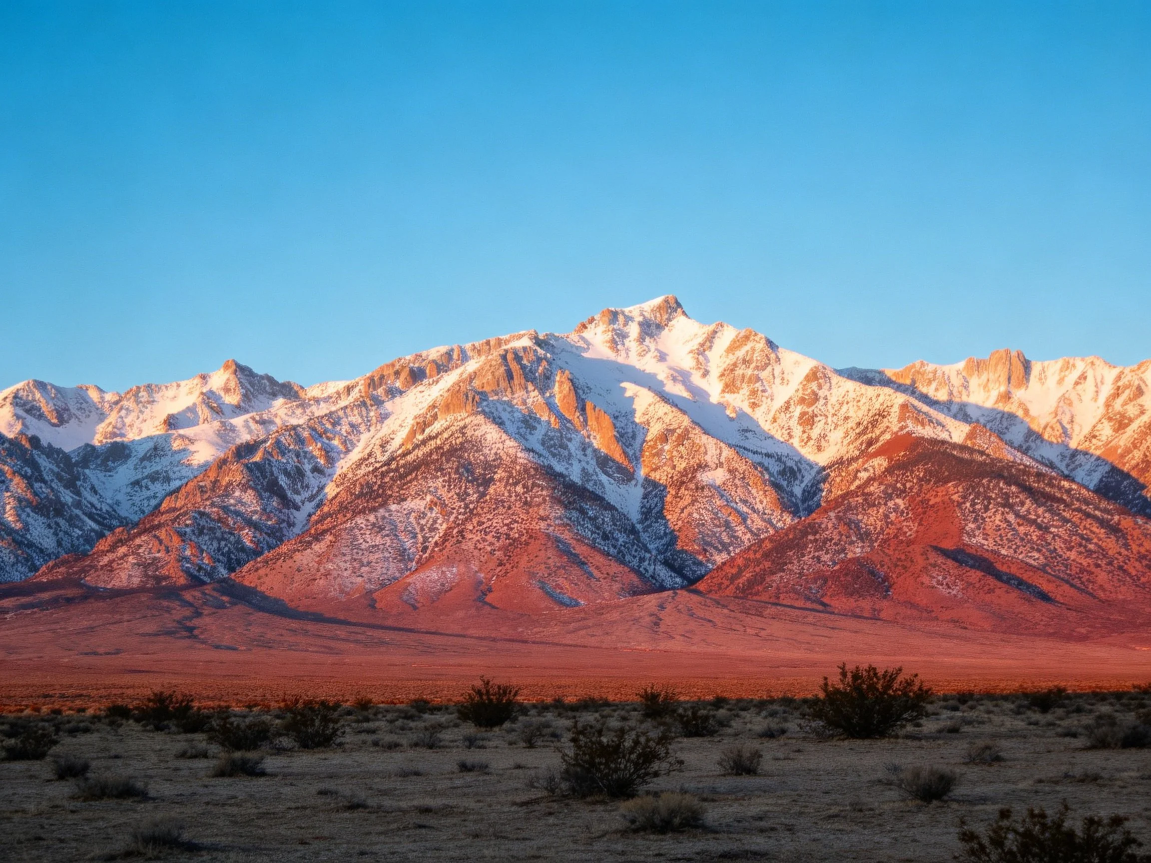 Snow-capped mountains glow under a clear blue sky with golden light
