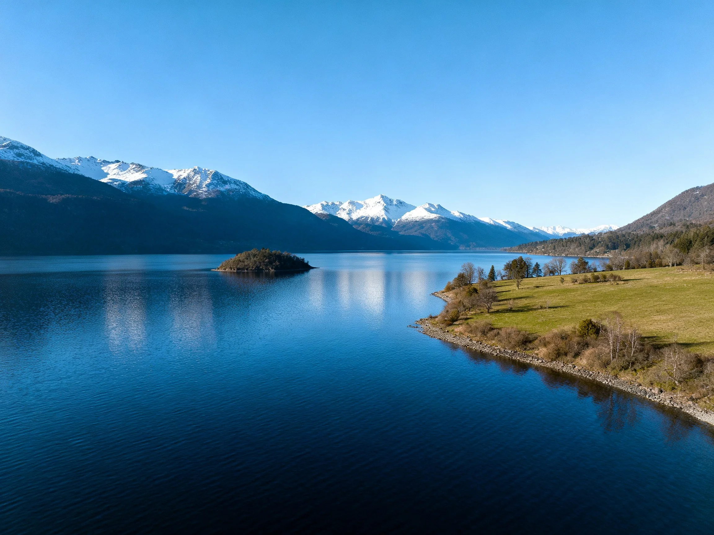 Snow-capped mountains overlook a calm blue lake with an island
