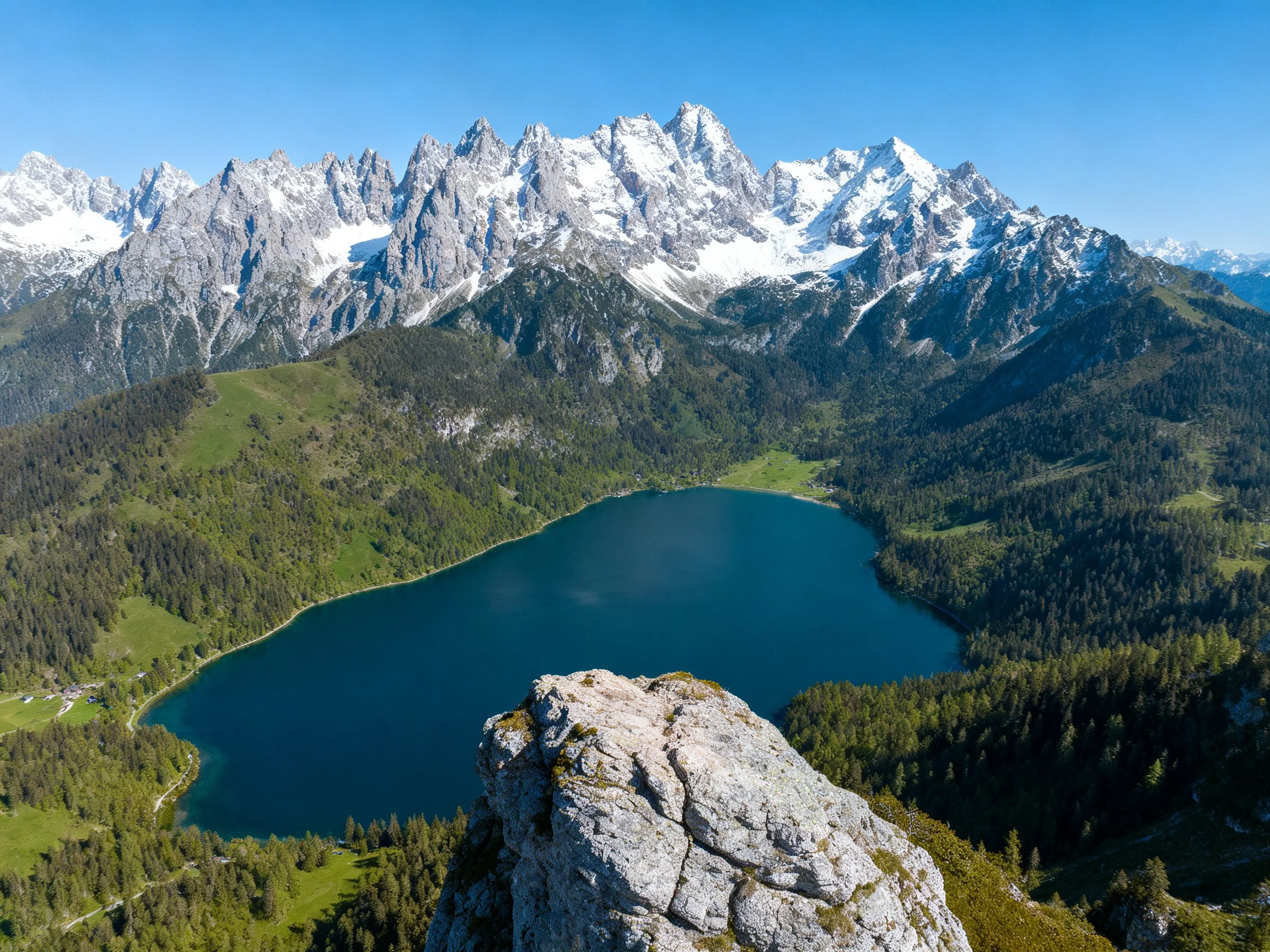 Snow-capped mountains overlook a deep blue alpine lake with forested slopes