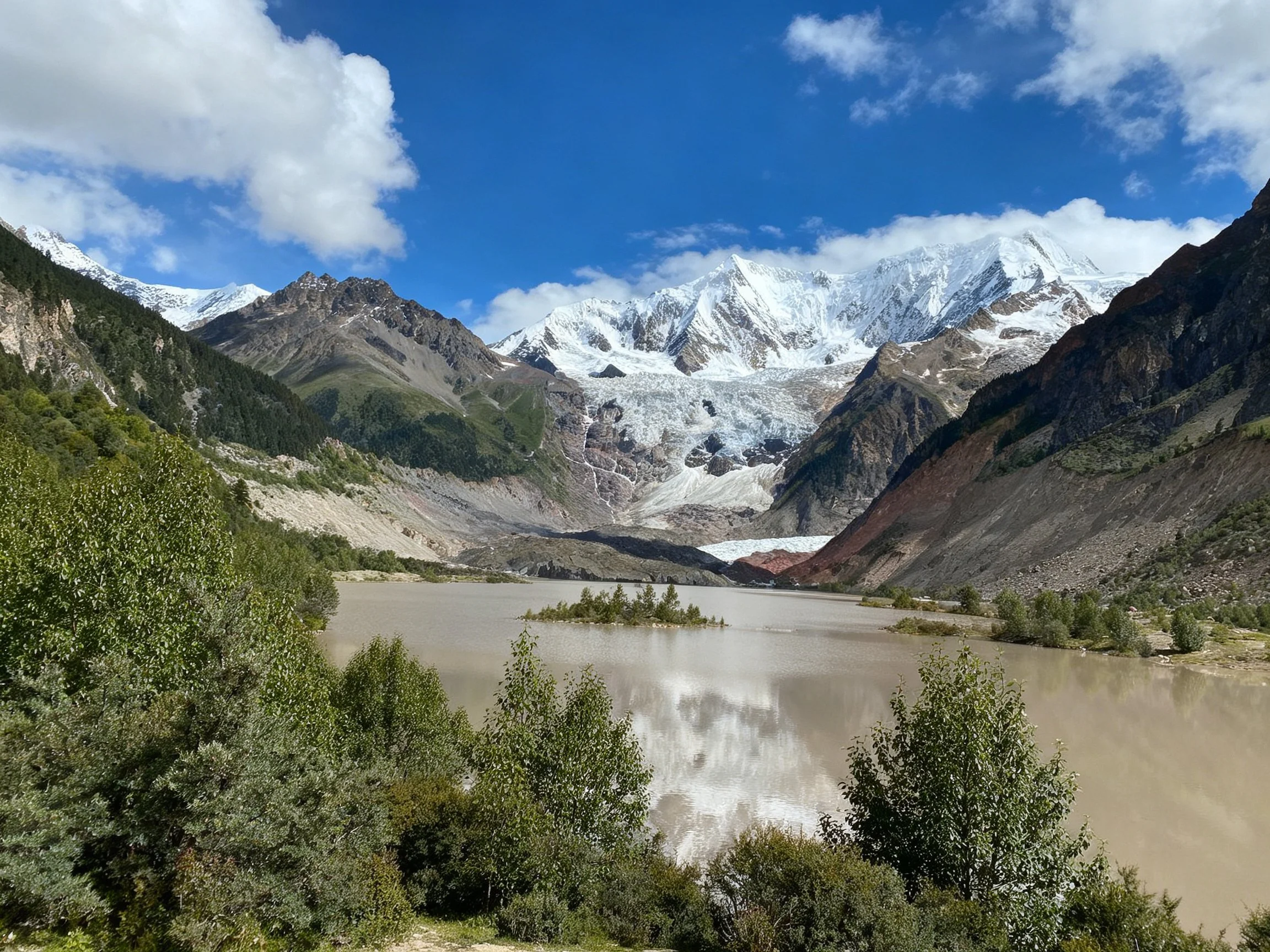 Snow - capped mountains overlook a glacial lake with lush green forests