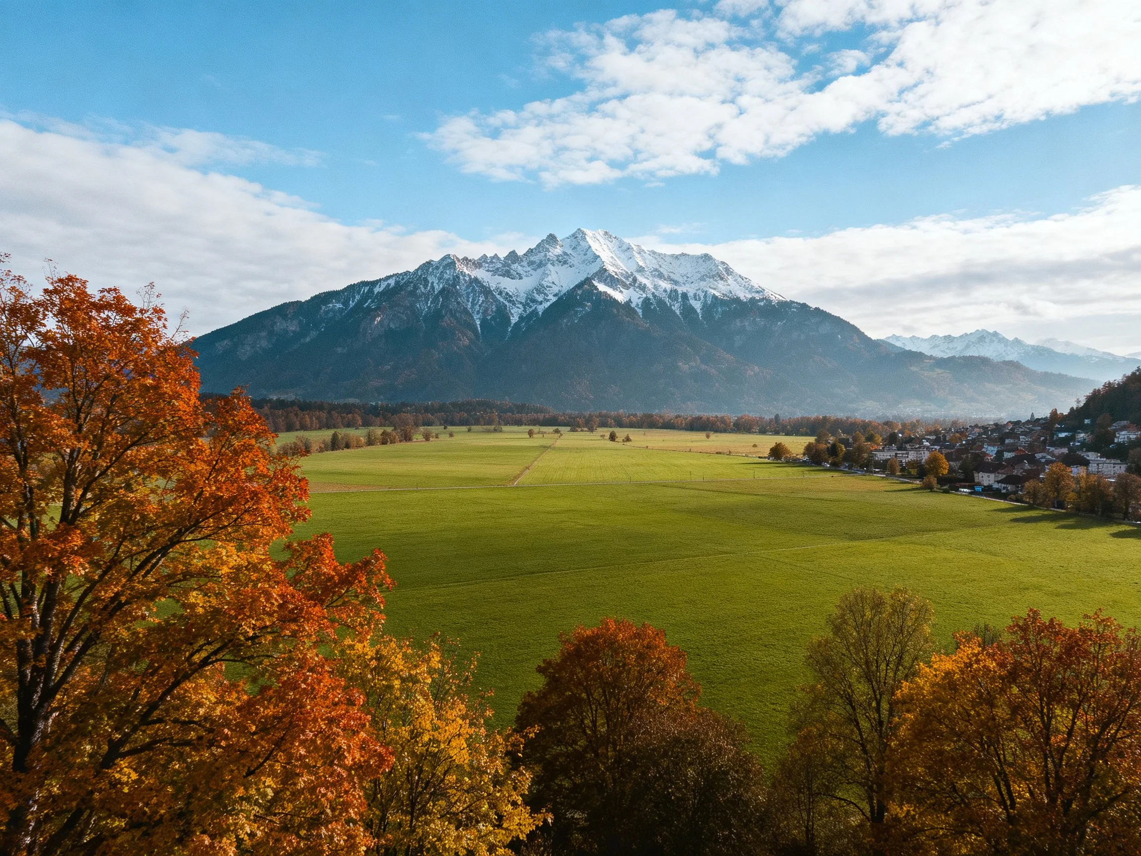 Snow-capped mountains overlook a lush green valley with autumn foliage