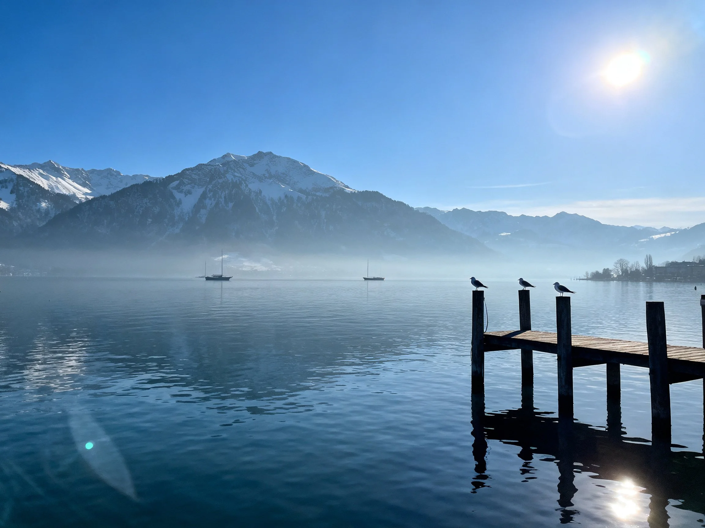 Snow-capped mountains overlook a misty lake with wooden dock