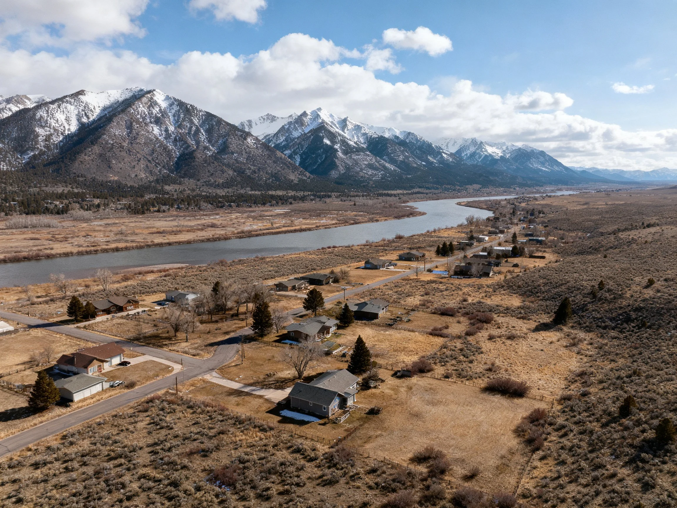 Snow-capped mountains overlook a winding river and scattered homes