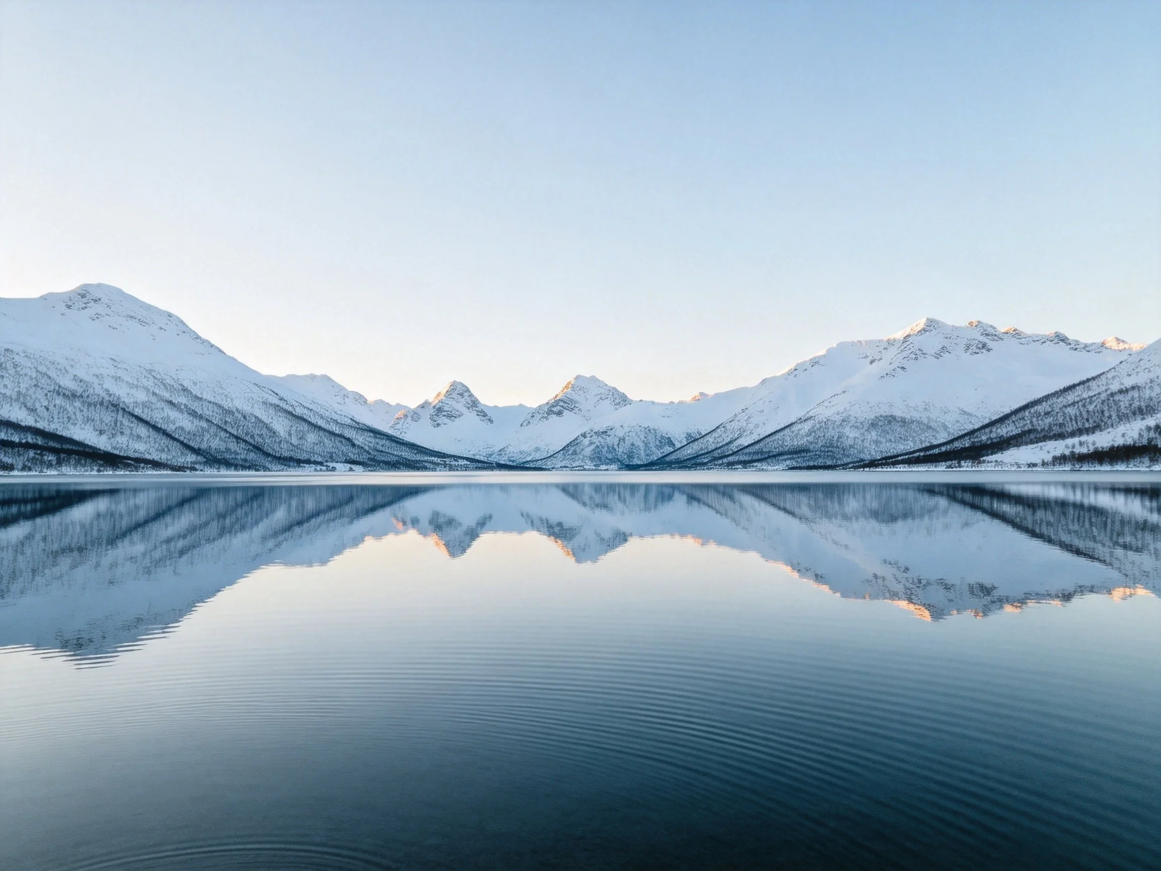 Snow - capped mountains reflect in a serene, blue - hued lake
