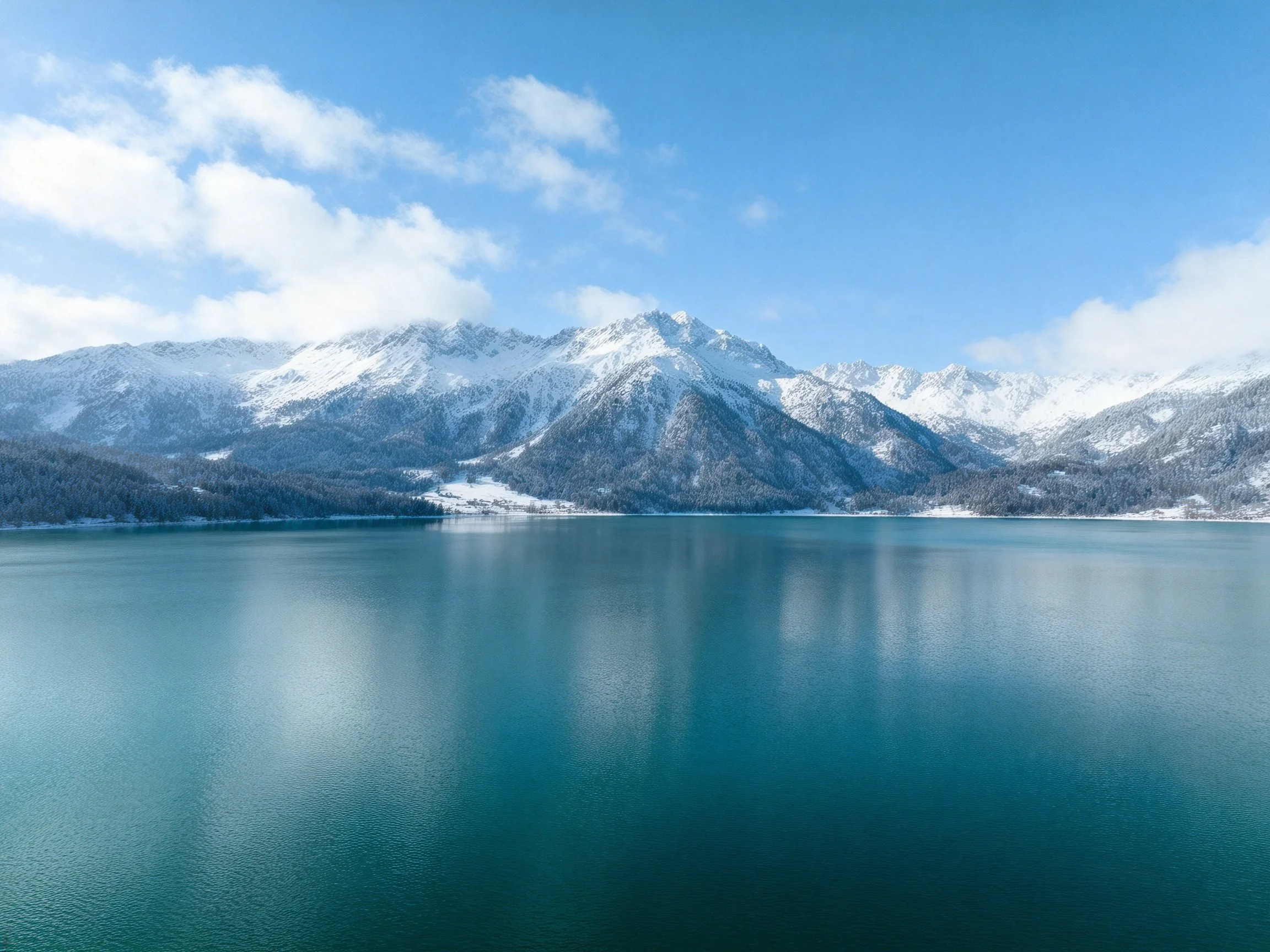 Snow - capped mountains reflect in a tranquil turquoise lake under bright blue sky