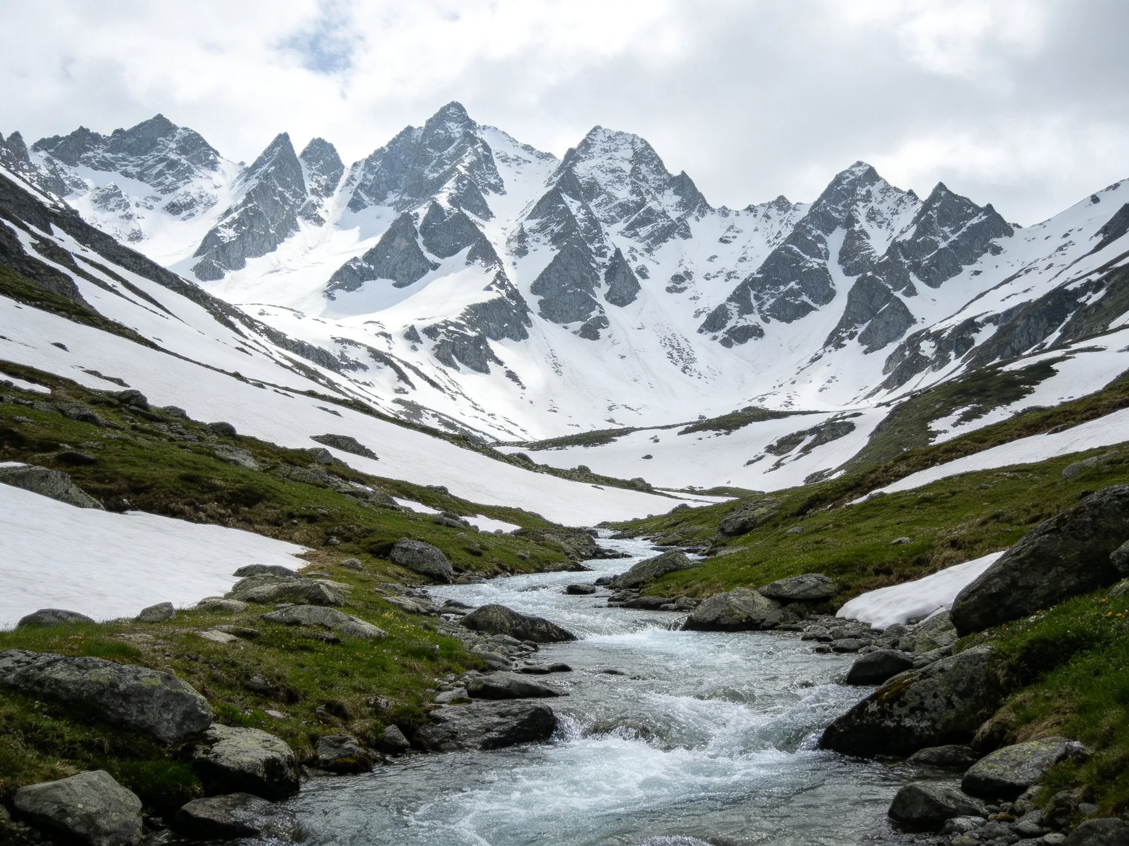 Snow-capped mountains tower over a rocky stream valley