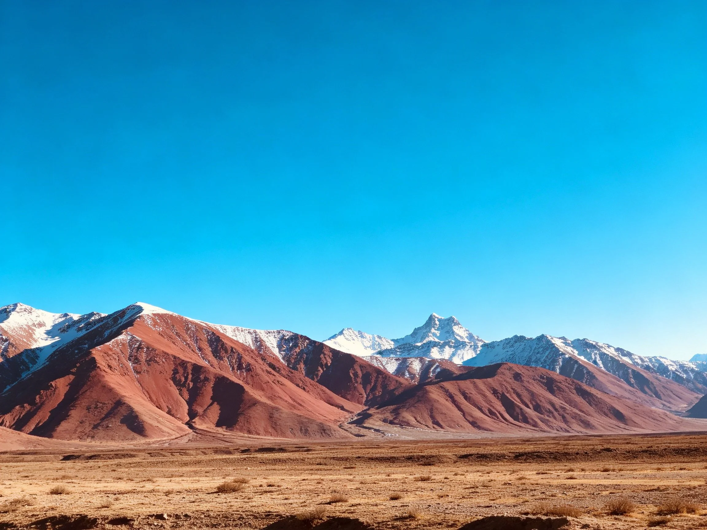 Snow-capped mountains with rust-hued slopes under a vivid blue sky