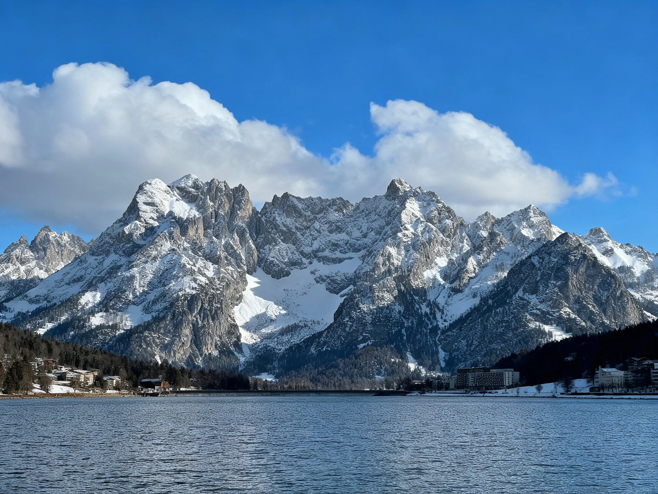 Snow-capped peaks rise behind a serene winter lake under bright blue skies