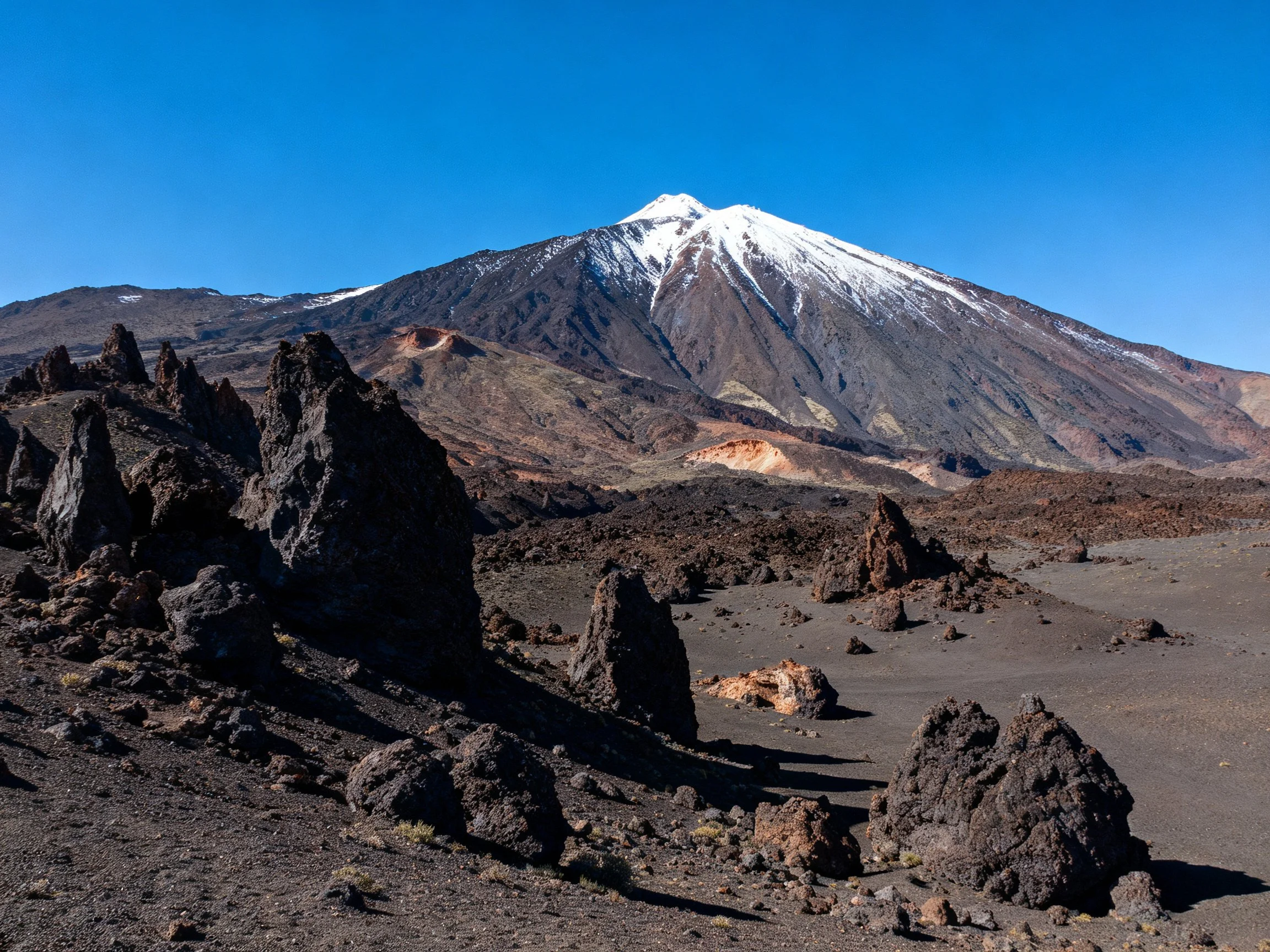 Snow-capped volcano with dark volcanic rock formations