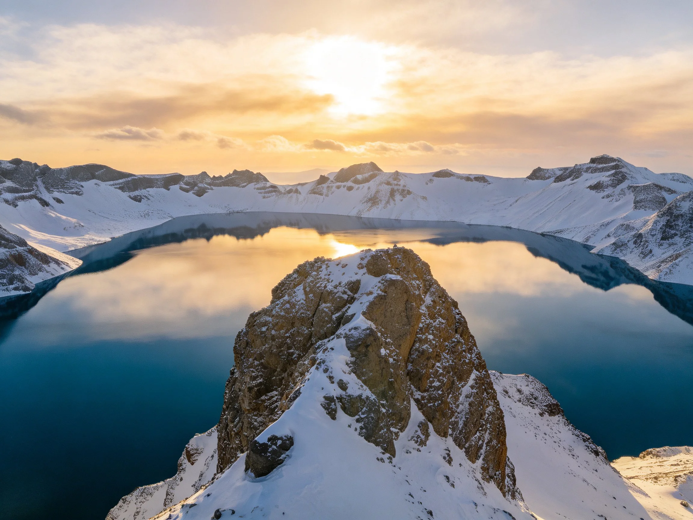 Snow-covered mountain crater lake reflecting golden sunlight