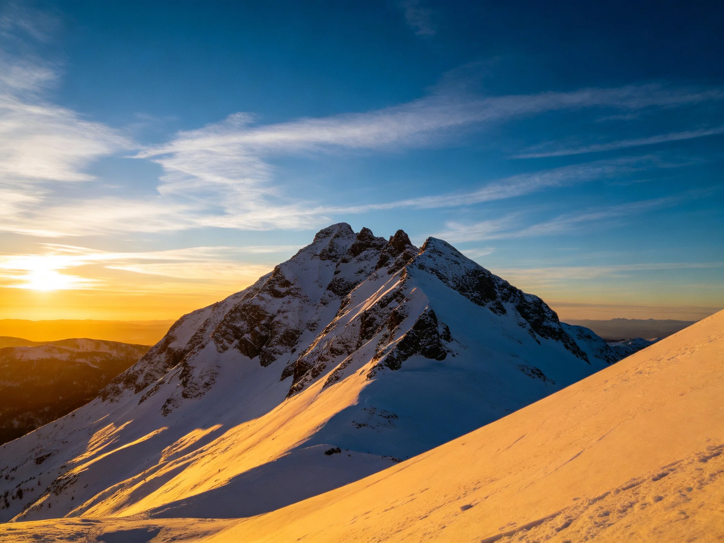 Snow - covered mountain peak bathed in golden sunset light