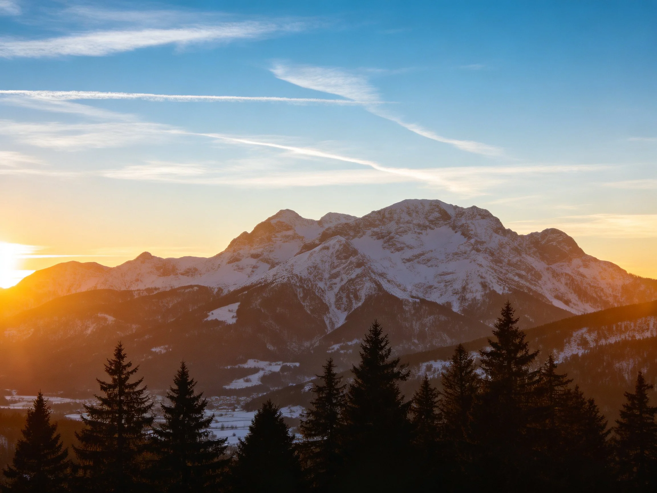 Snow - covered mountain peaks at golden sunset with pine forest