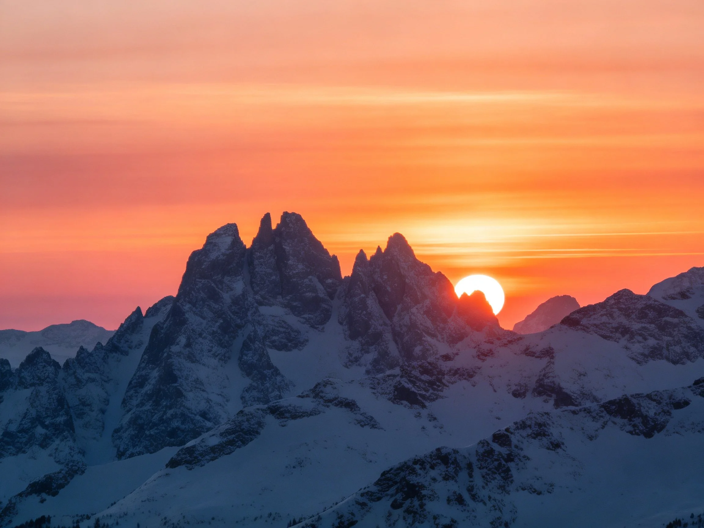 Snow-covered mountain peaks beneath a vivid orange sunset sky
