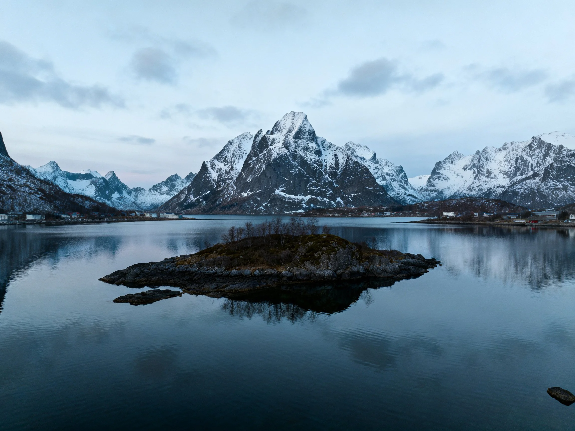 Snow covered mountain peaks overlook calm waters with a central island