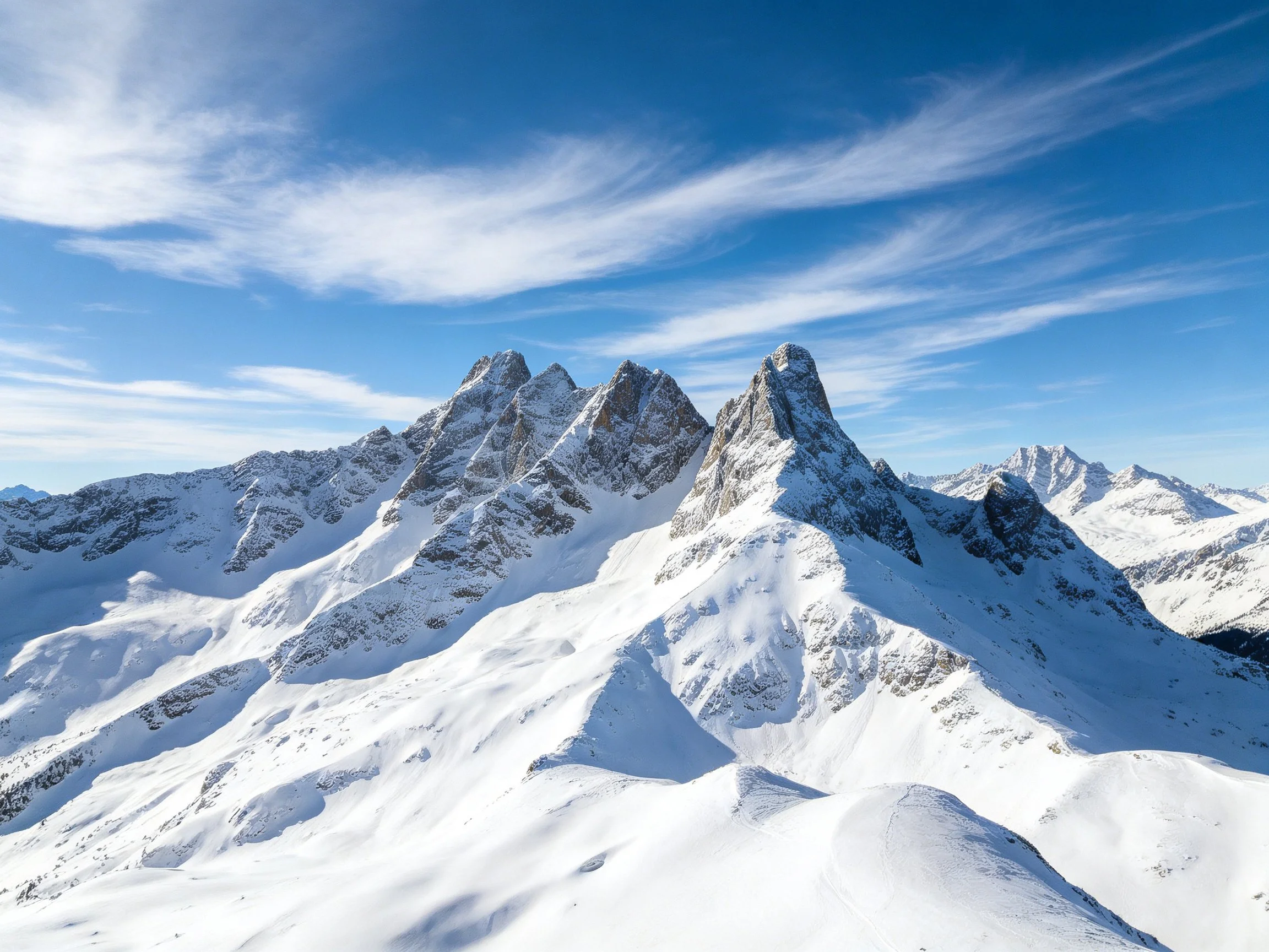 Snow-covered mountain peaks under bright blue sky with wispy clouds