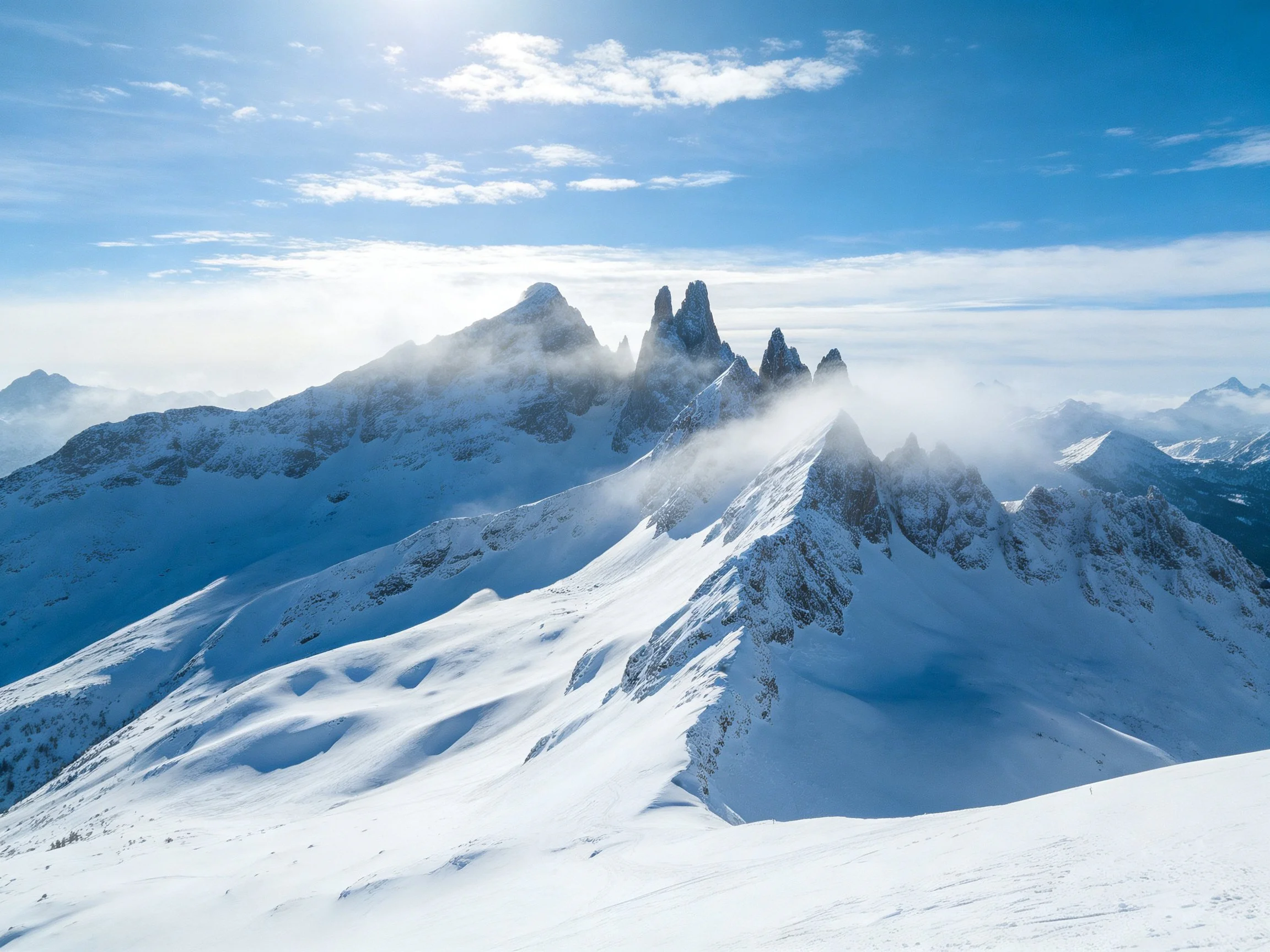Snow-covered mountain peaks with clear blue skies and misty clouds