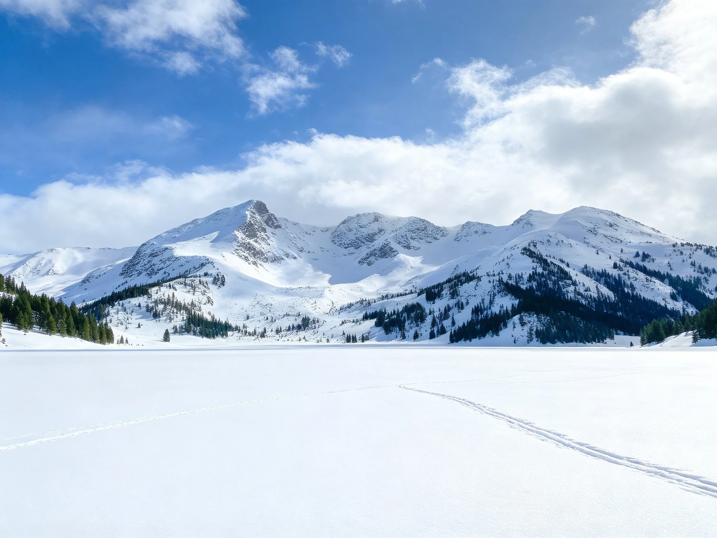 Snow-covered mountain range with frozen lake and evergreen forests