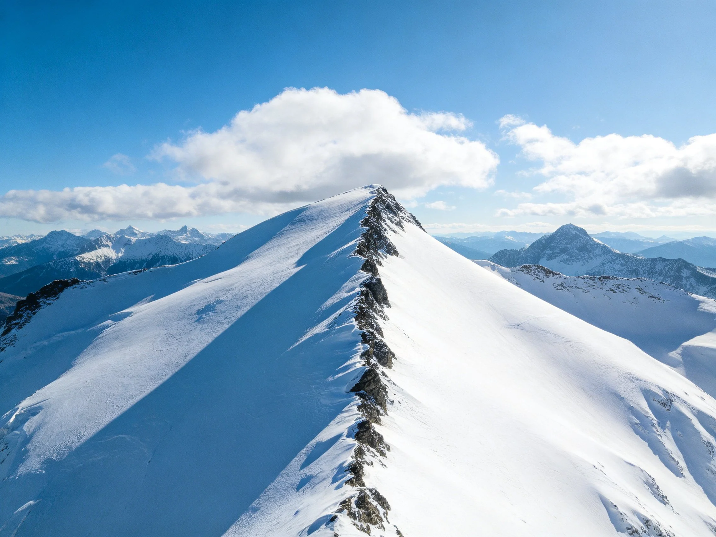 Snow-covered mountain ridge with rocky summit and clear blue sky