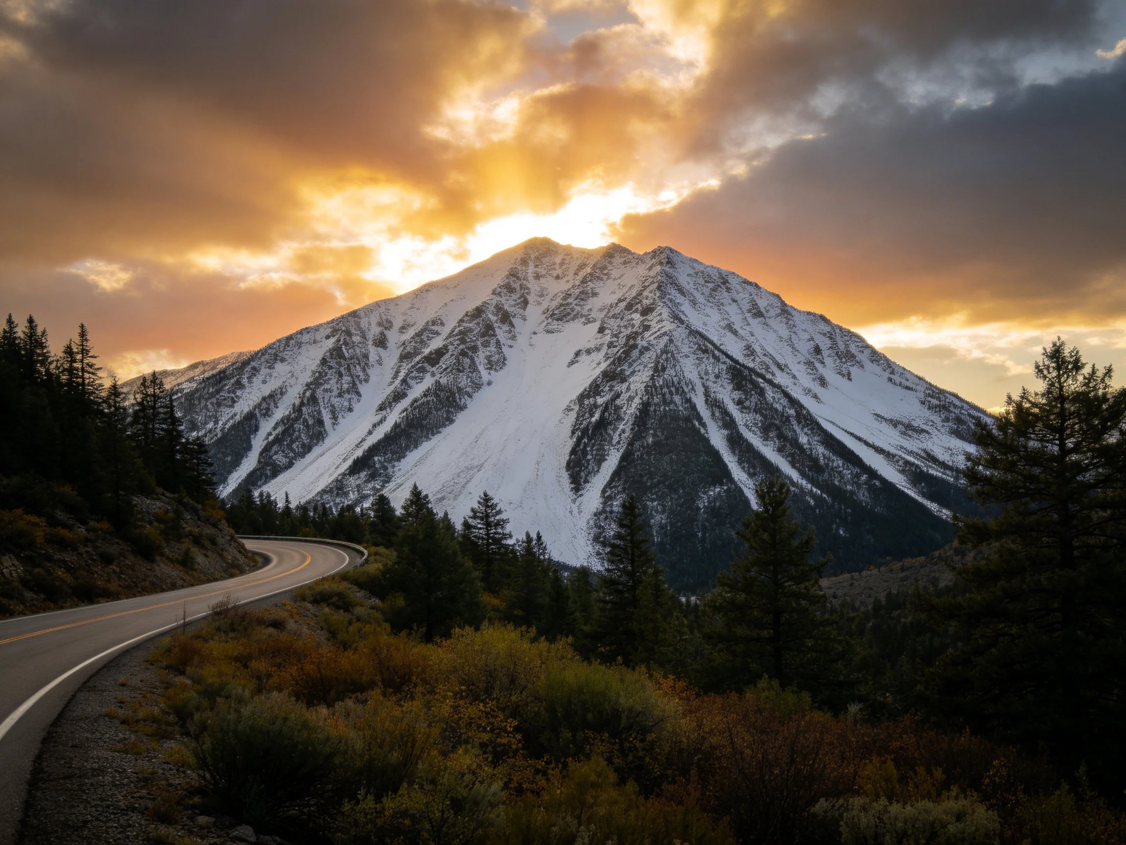 Snow - covered mountain with winding road under golden sunset sky