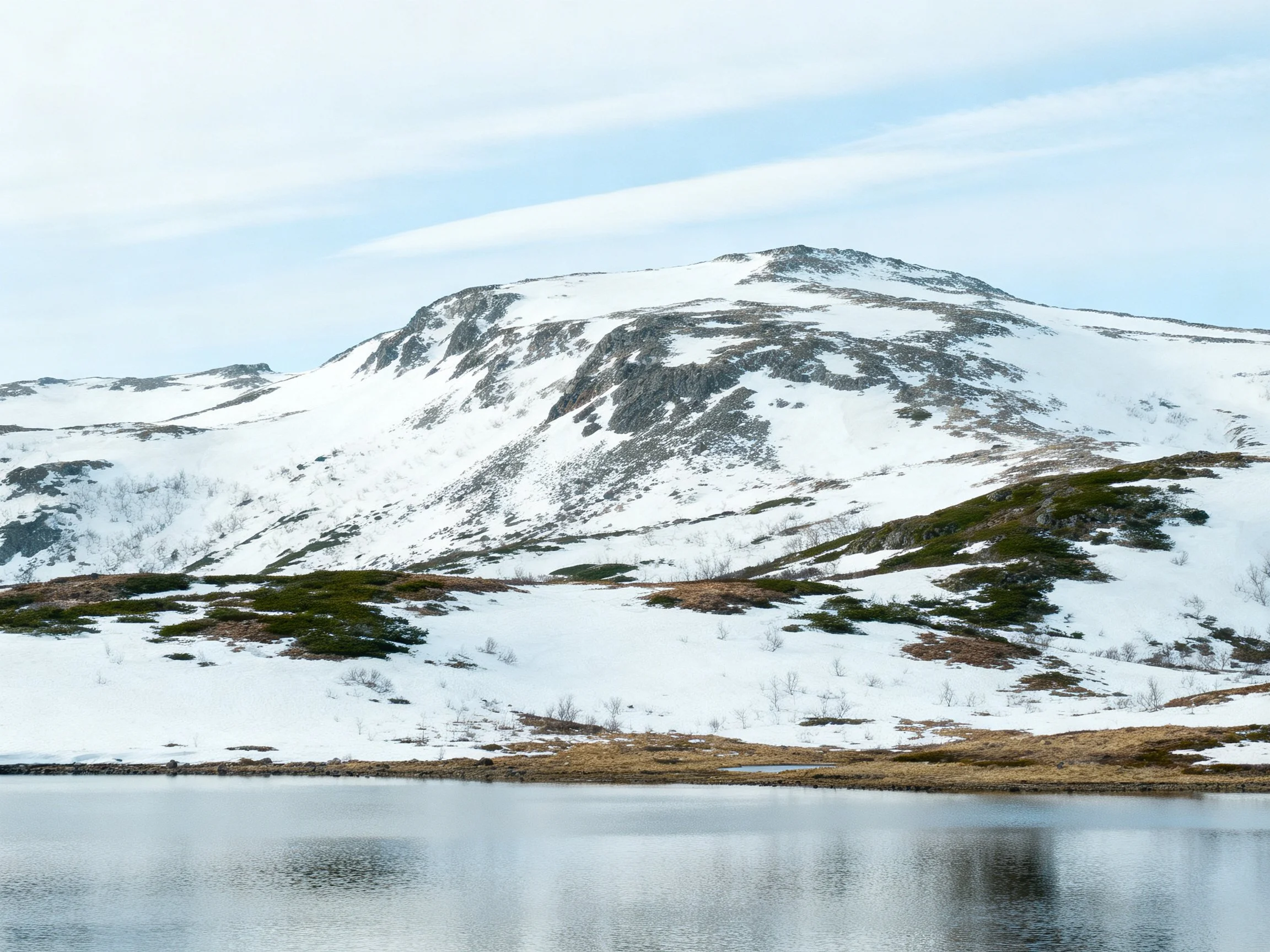 Snow-draped mountain with rocky outcrops and a serene lake