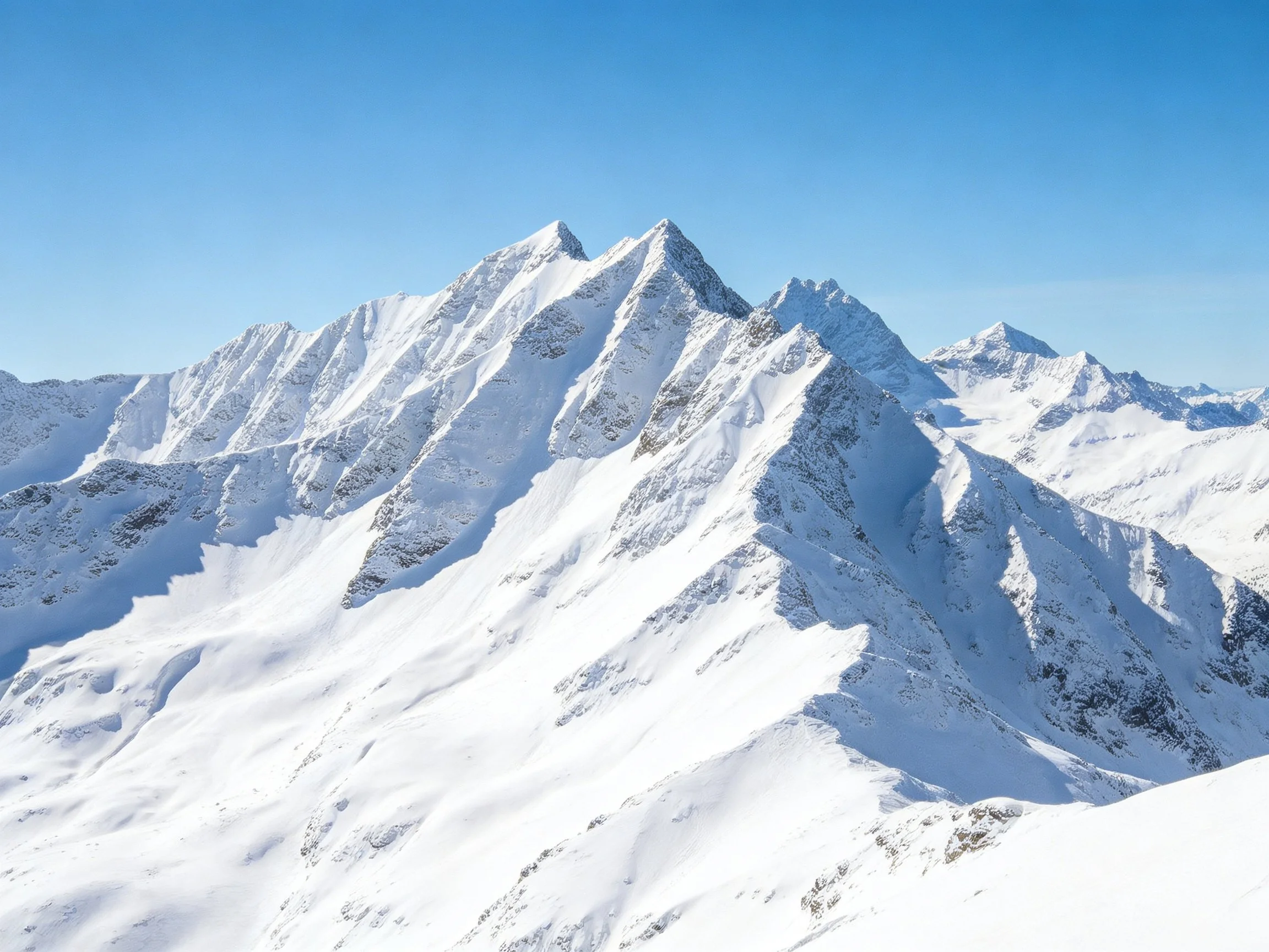 Snowy mountain peaks with sharp ridges under clear blue sky