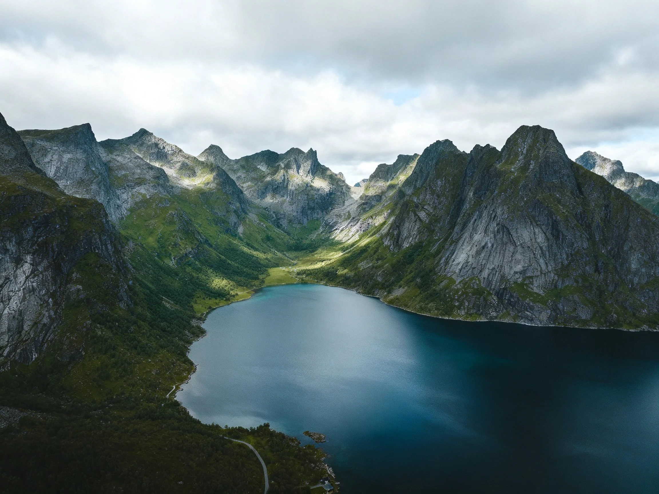Steep gray mountains frame a deep blue lake with green slopes.