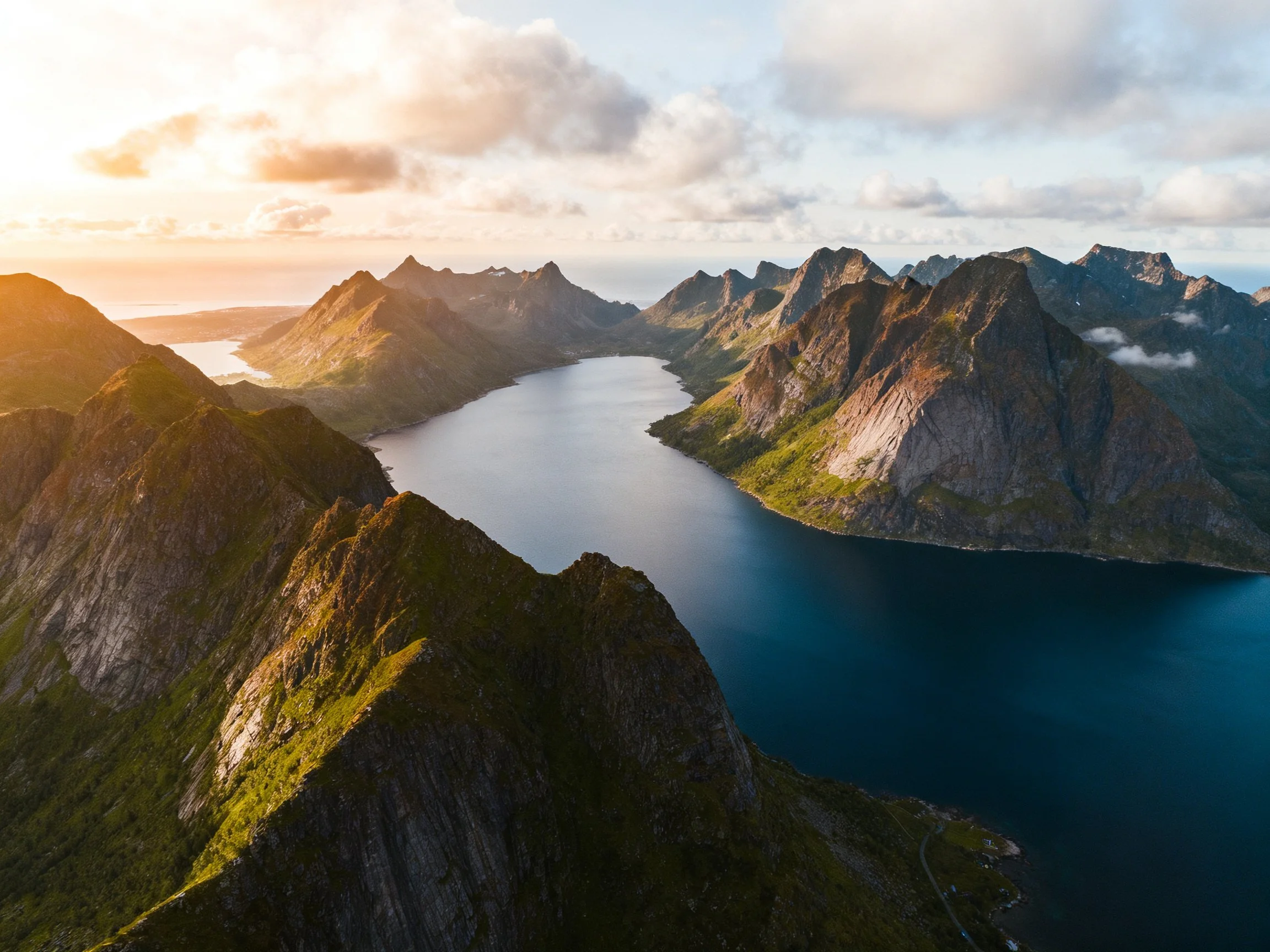 Steep rocky peaks frame a deep blue fjord during golden hour