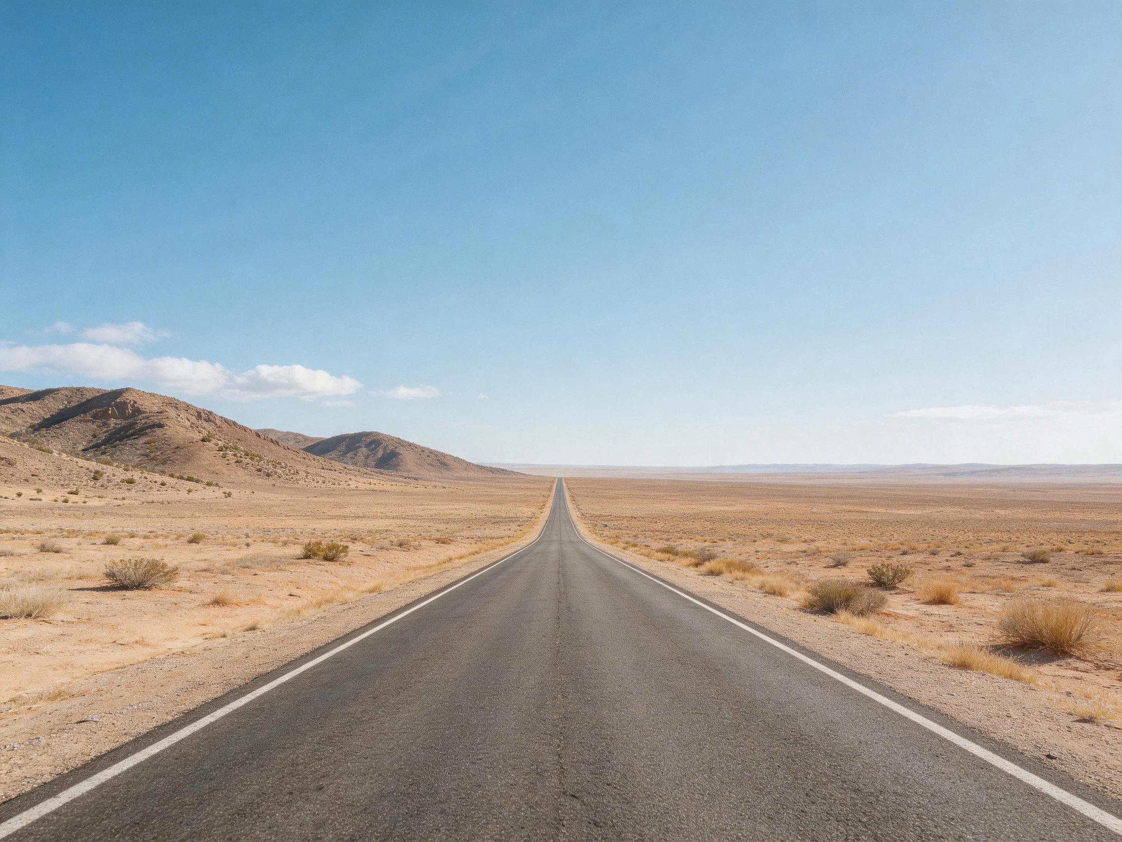 Straight asphalt road stretches into vast desert near distant mountains