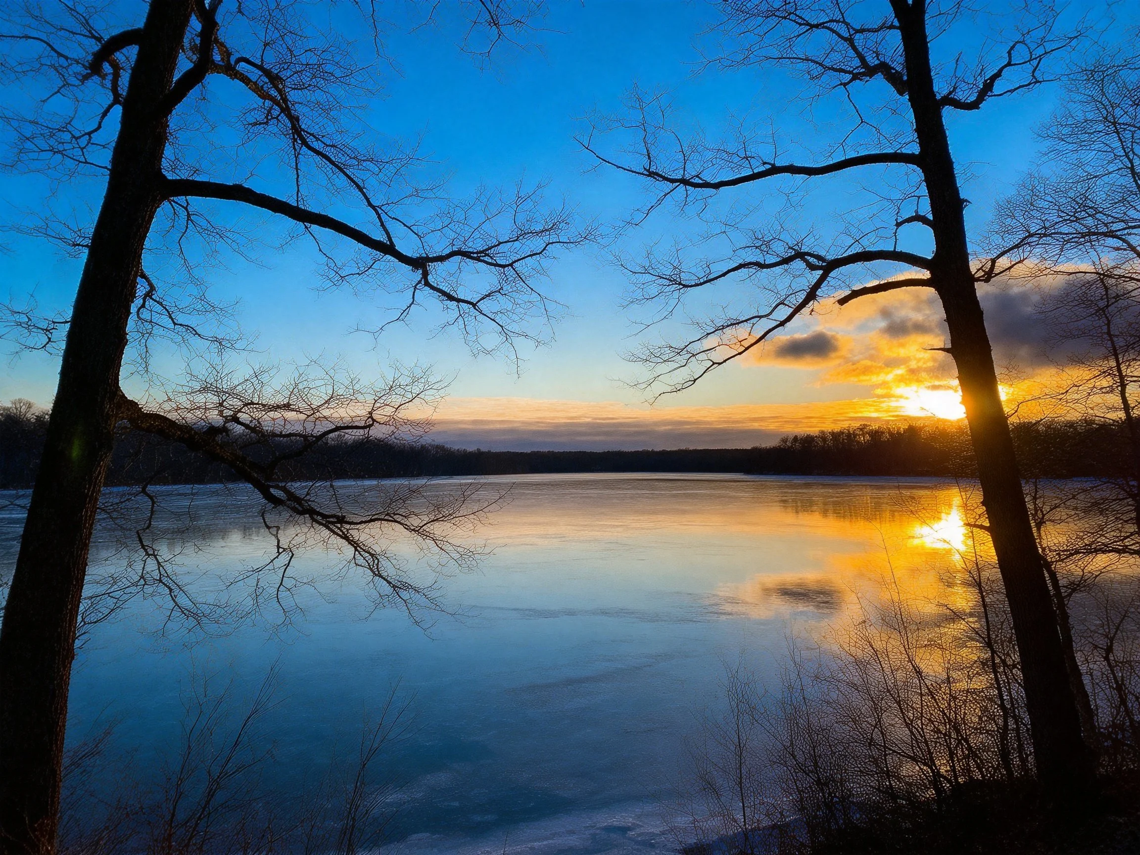 Sunset Over Frozen Lake With Silhouetted Trees